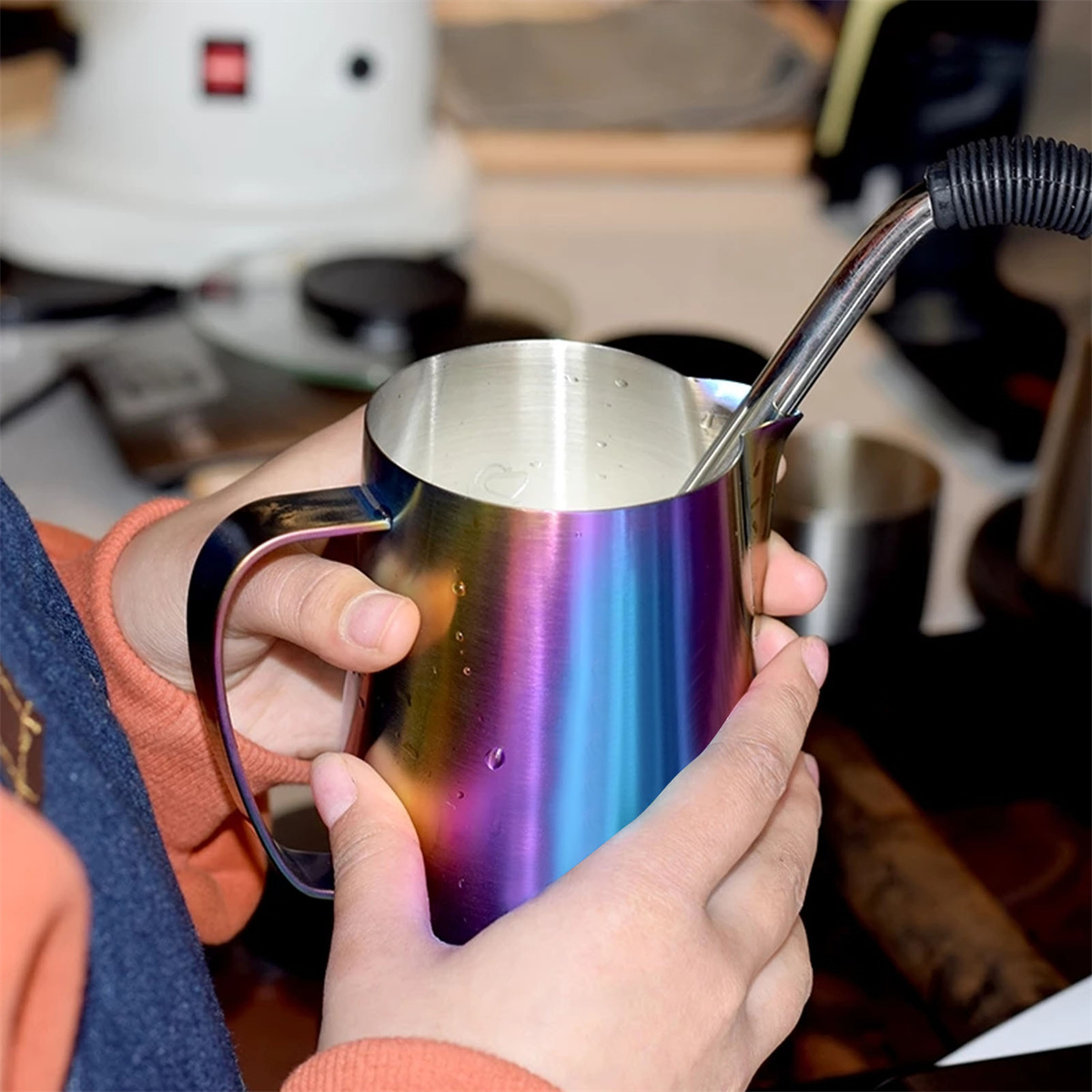 Eine Person hält eine regenbogenfarbene Milchaufschäumkanne.
