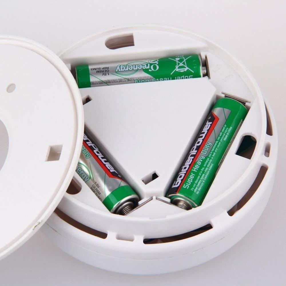 Ein Rauchmelder mit drei grünen Batterien im Inneren. Der Detektor ist weiß mit offenem Deckel.