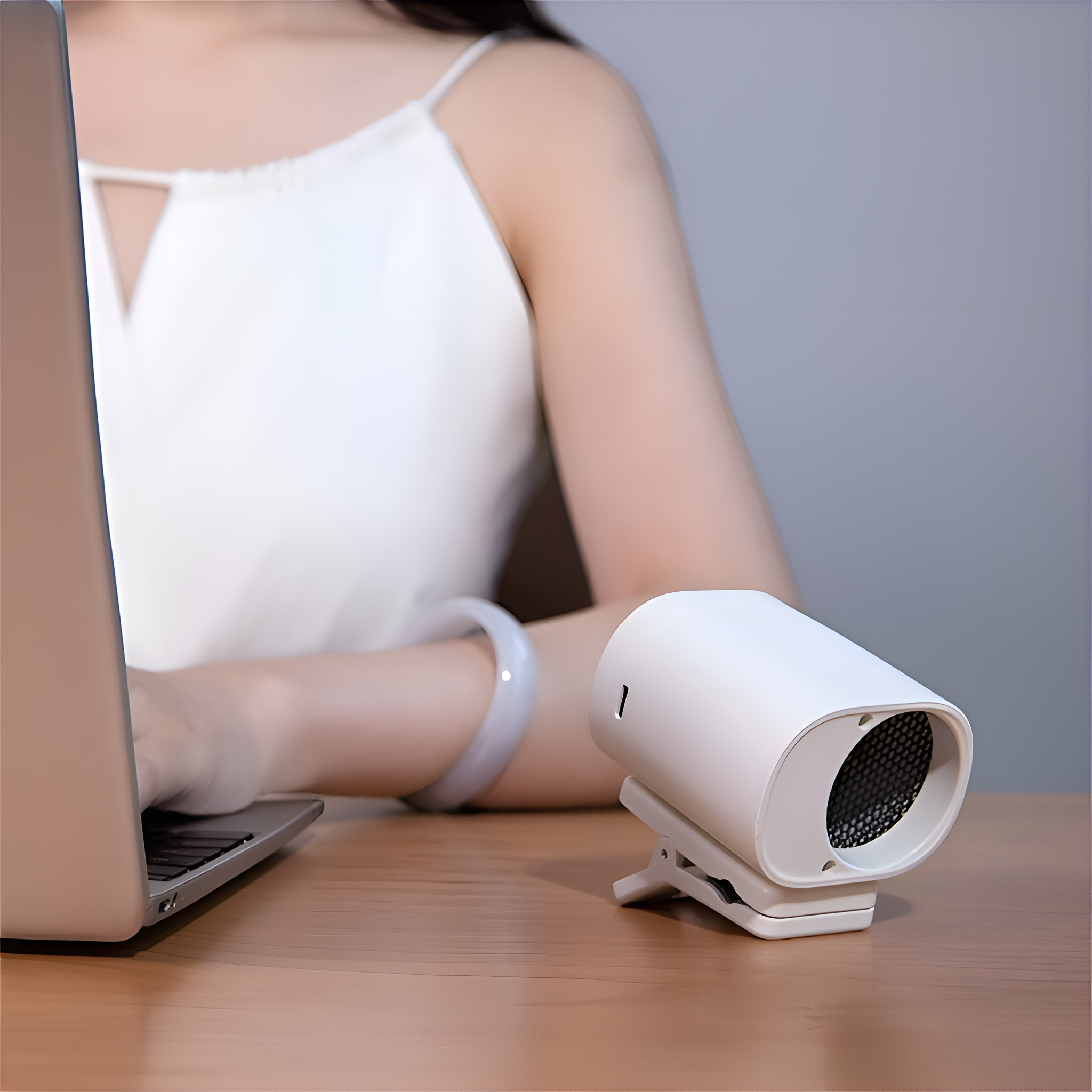 Frau benutzt Laptop, weißer Mini-Ventilator auf dem Tisch. Der Ventilator ist vor ihr.