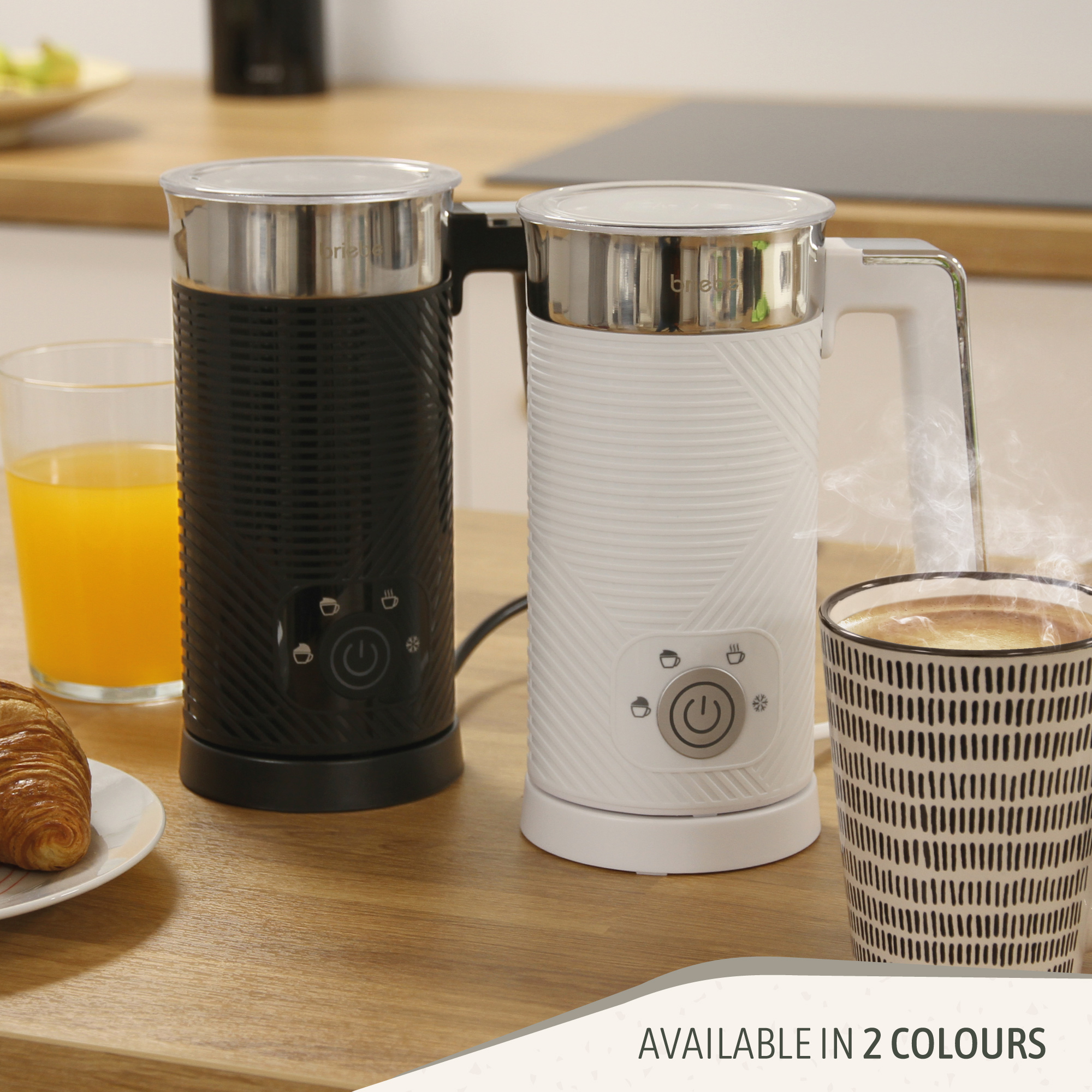 Zwei elektrische Milchaufschäumer, einer schwarz und einer weiß, neben einer Tasse Kaffee und einem Croissant.