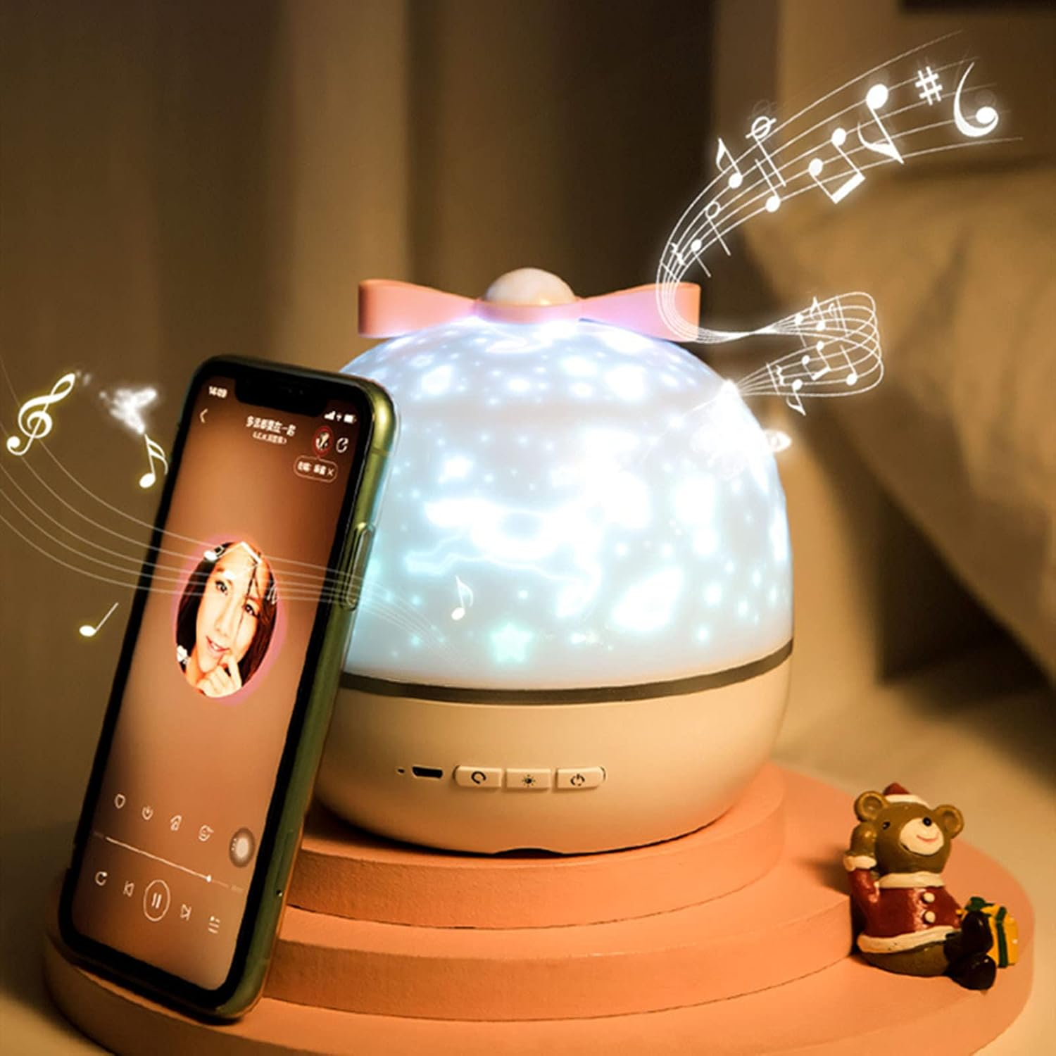 Eine Nachttischlampe mit Schleife, ein Musik abspielendes Telefon und eine Bärenfigur auf einem rosa Ständer.