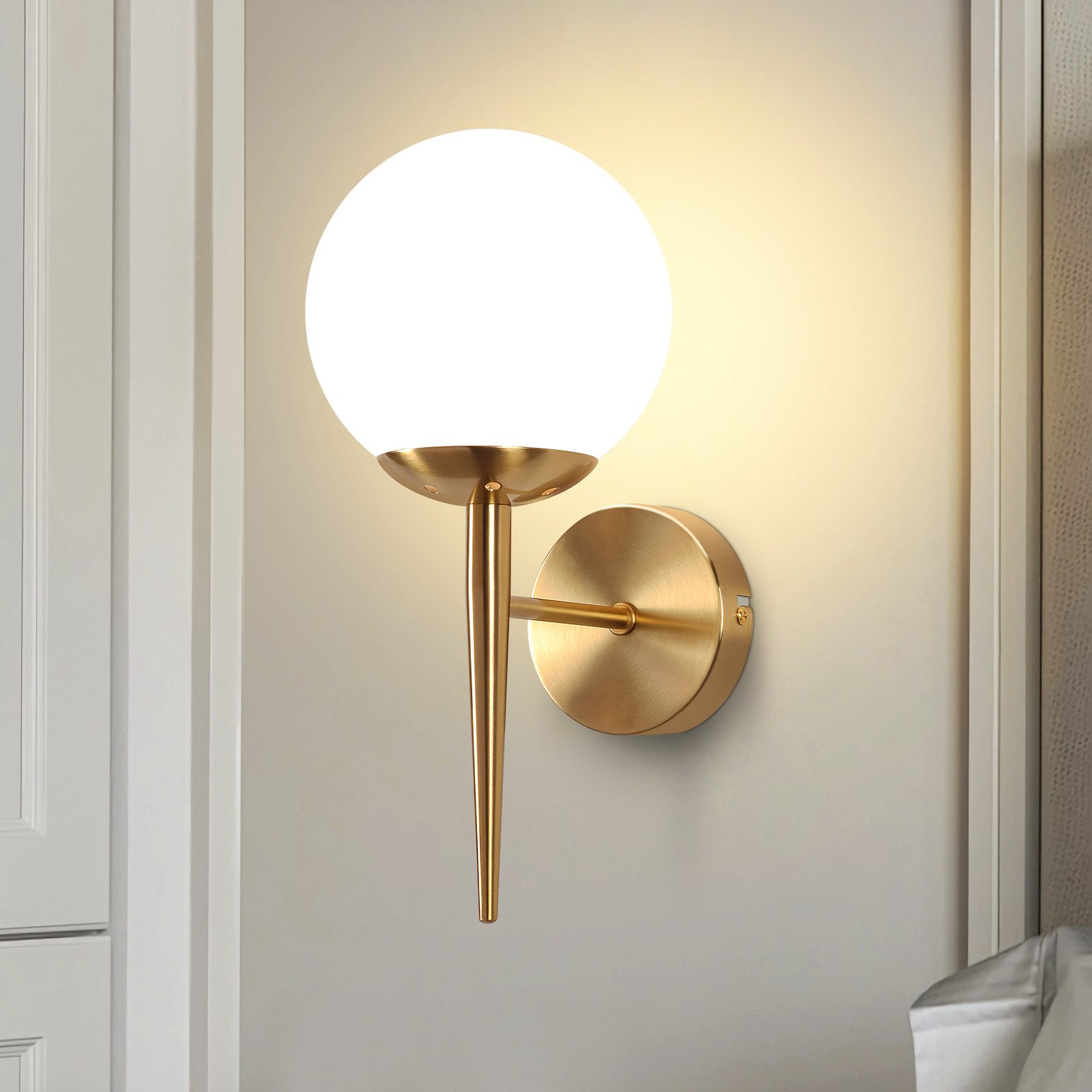Un'applique da parete con una lampada a globo bianca e uno stelo e base color oro.