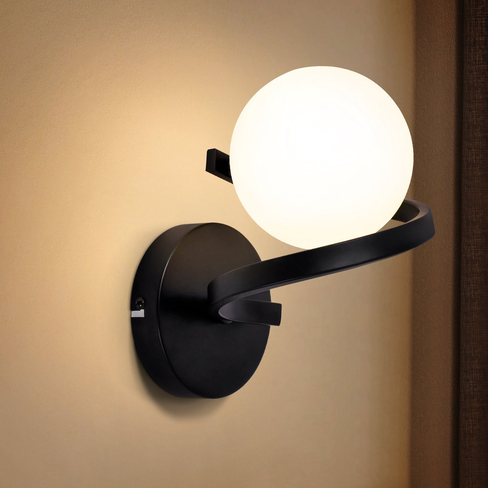 Una lampada nera a parete con un globo bianco e un braccio curvo. È illuminata e montata su una parete beige.