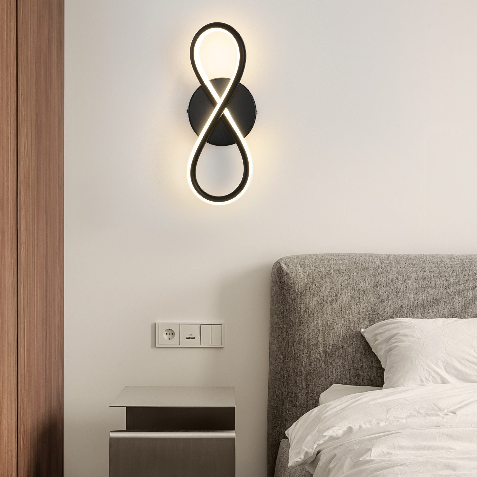 Applique a forma di simbolo dell'infinito, nero con luce bianca, montata su una parete bianca vicino a un letto.
