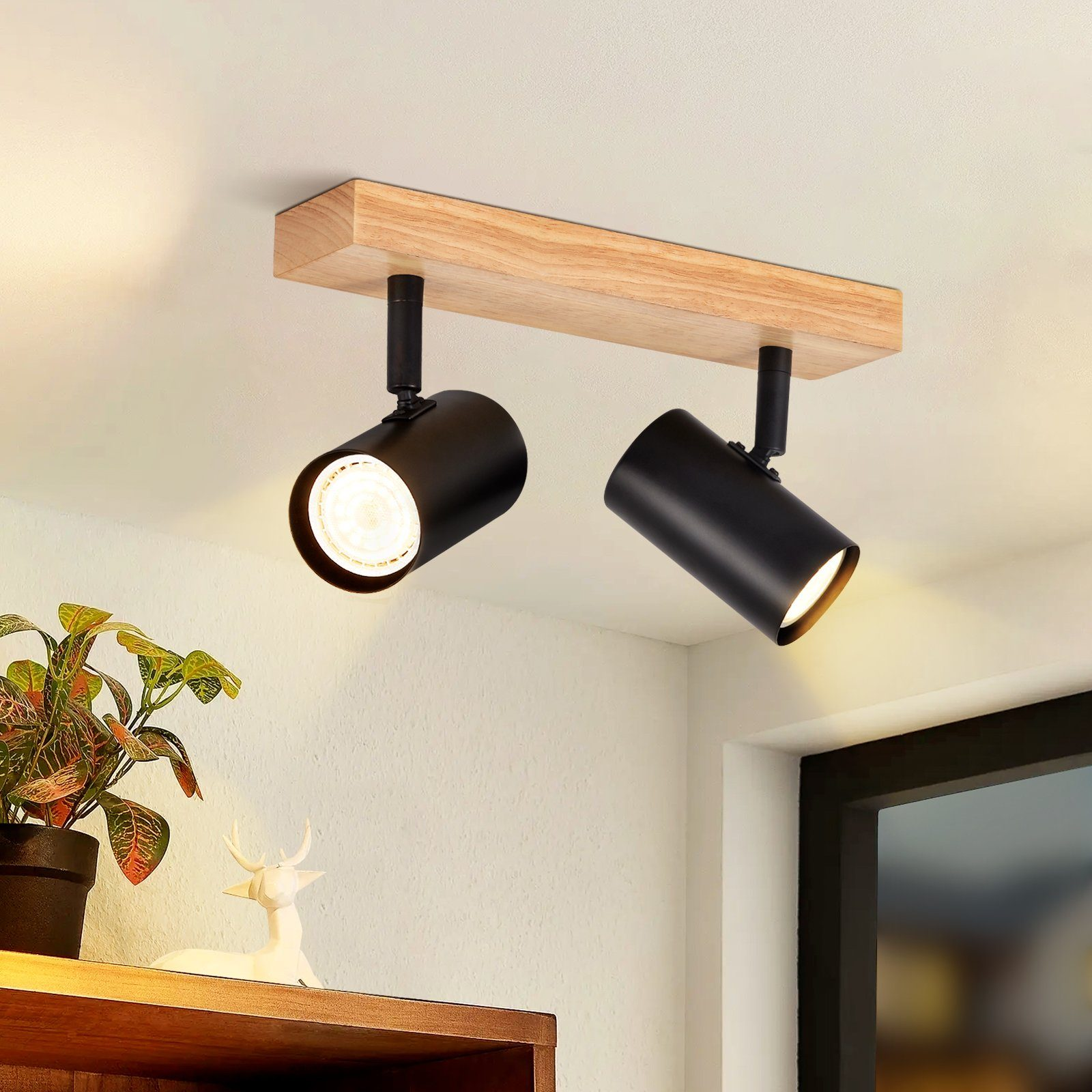 Due faretti neri su una trave di legno, fissati a un soffitto bianco, illuminati.