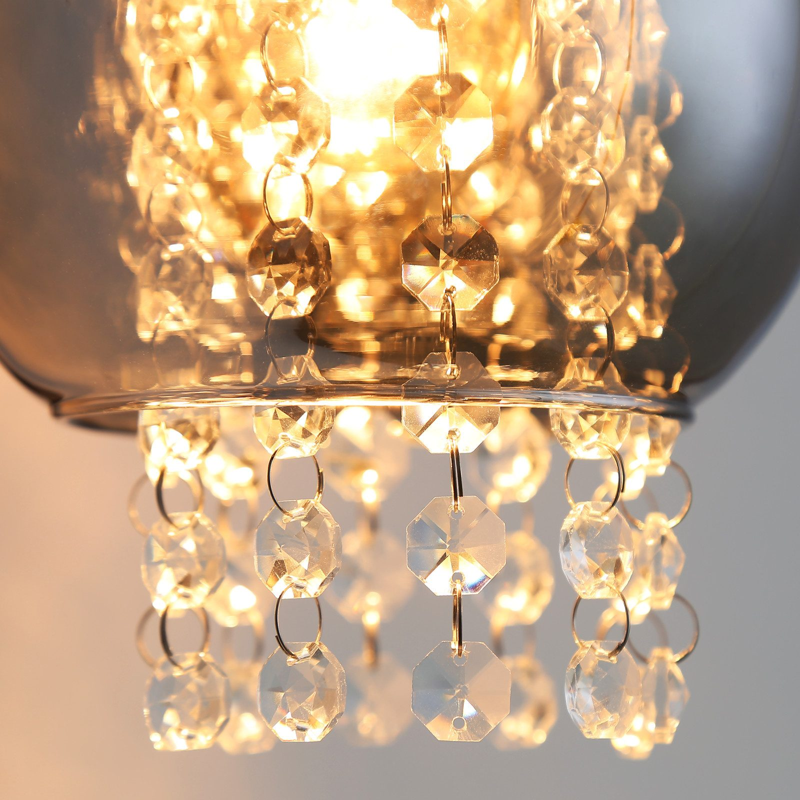 Primo piano di un lampadario con fili di cristallo e una sfera di vetro, la luce brilla attraverso.