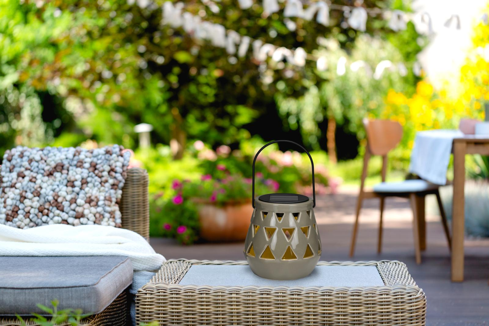 Une lanterne sur une table dans un jardin. Fond flou avec des plantes, une table et une chaise.