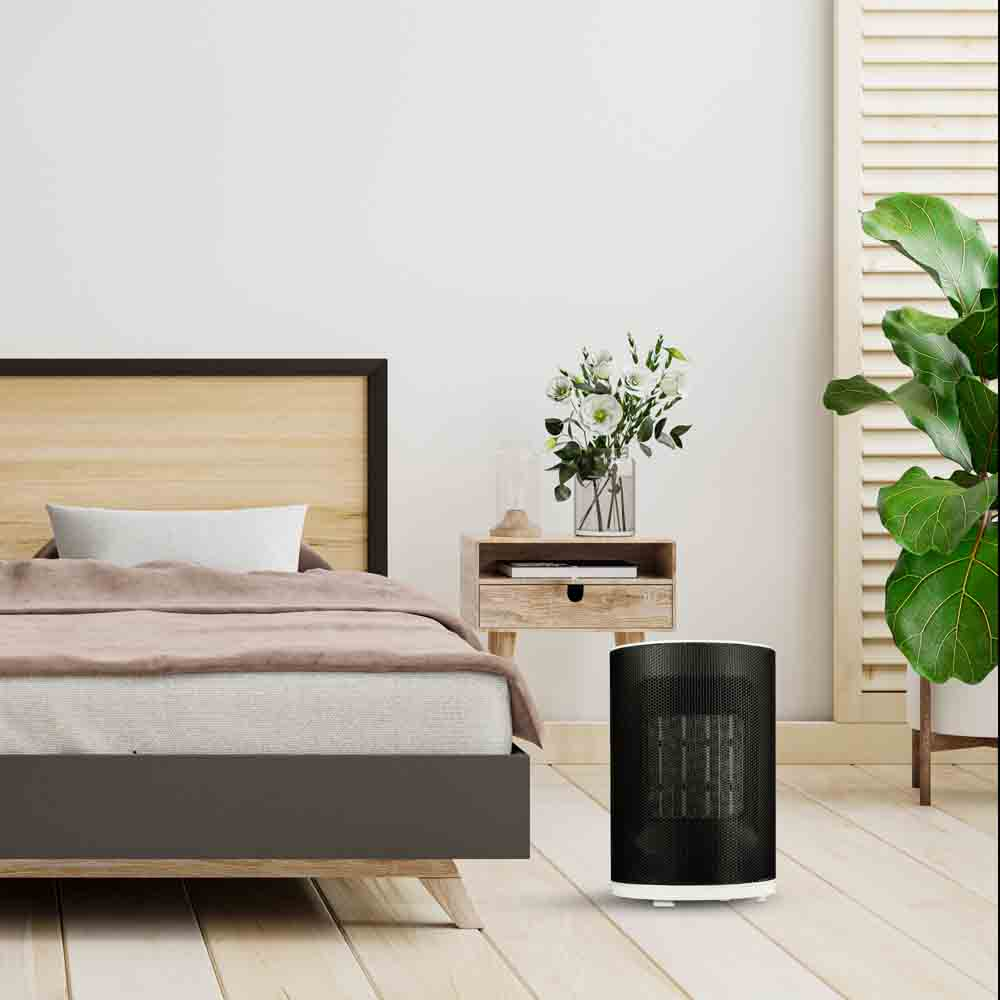 Escena de dormitorio: cama, calefactor, flores, suelo de madera. Pared y puerta blancas.