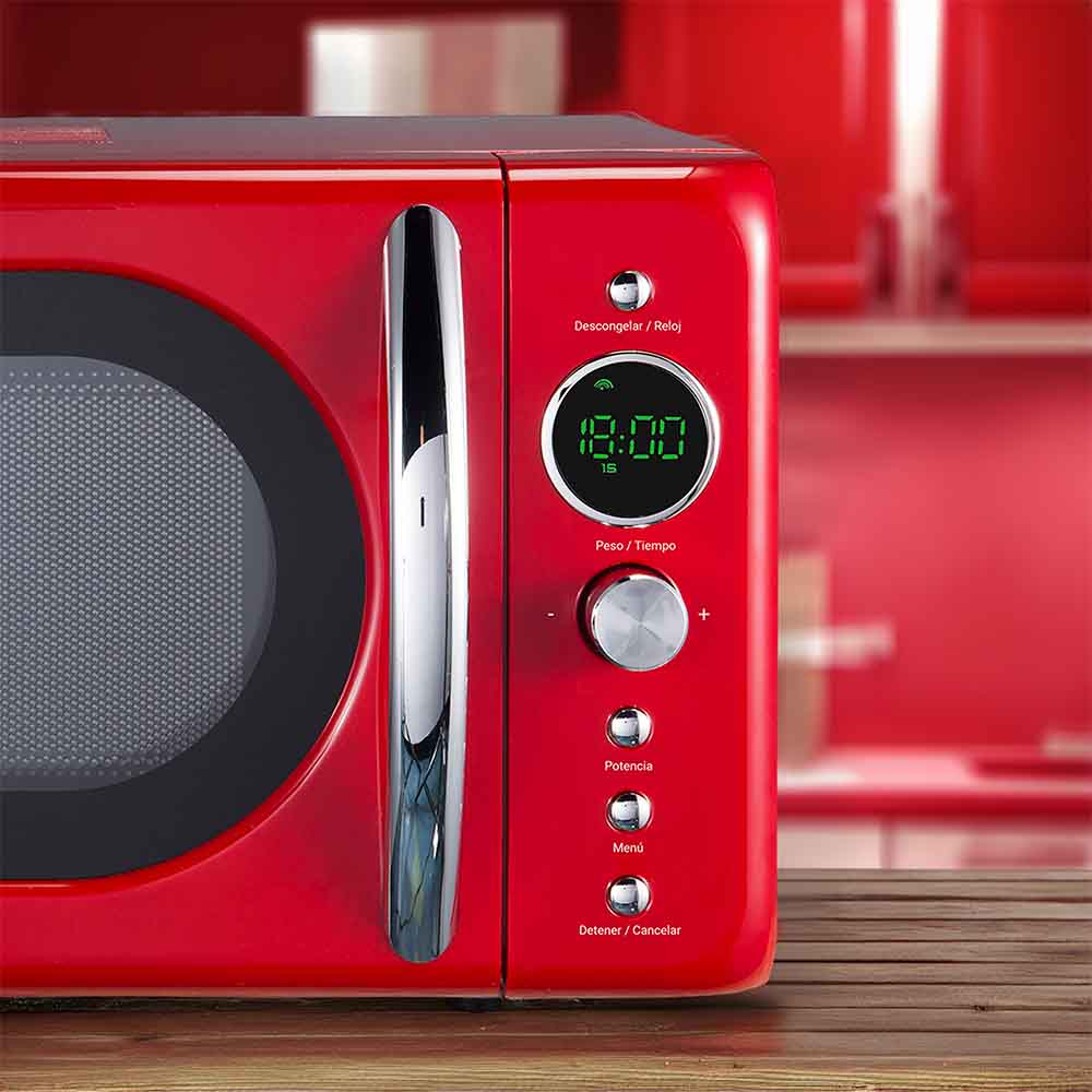Un microondas rojo con pantalla digital y botones sobre superficie de madera, fondo rojo.