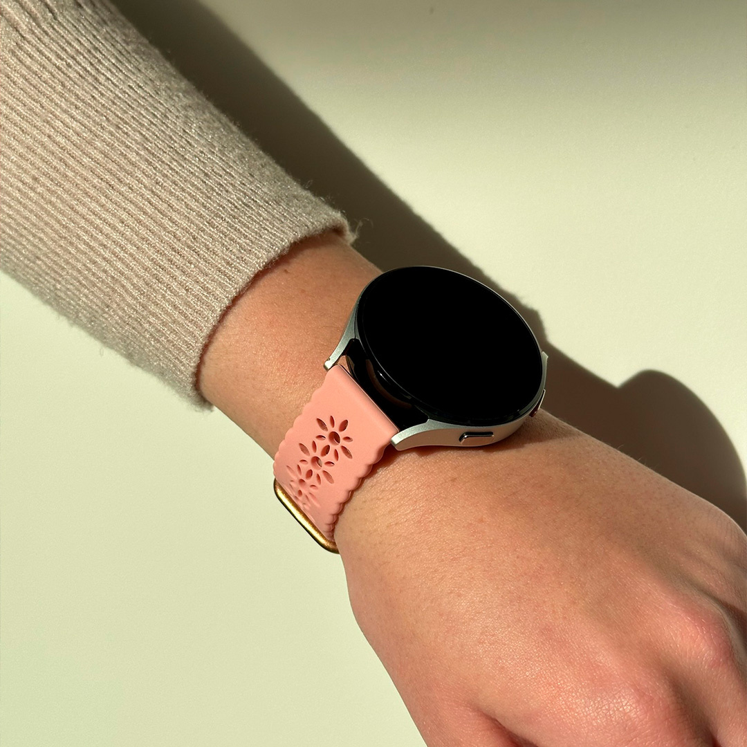 Handgelenk einer Frau mit Smartwatch. Rosa Uhrenarmband mit Löchern, schwarzer Bildschirm.