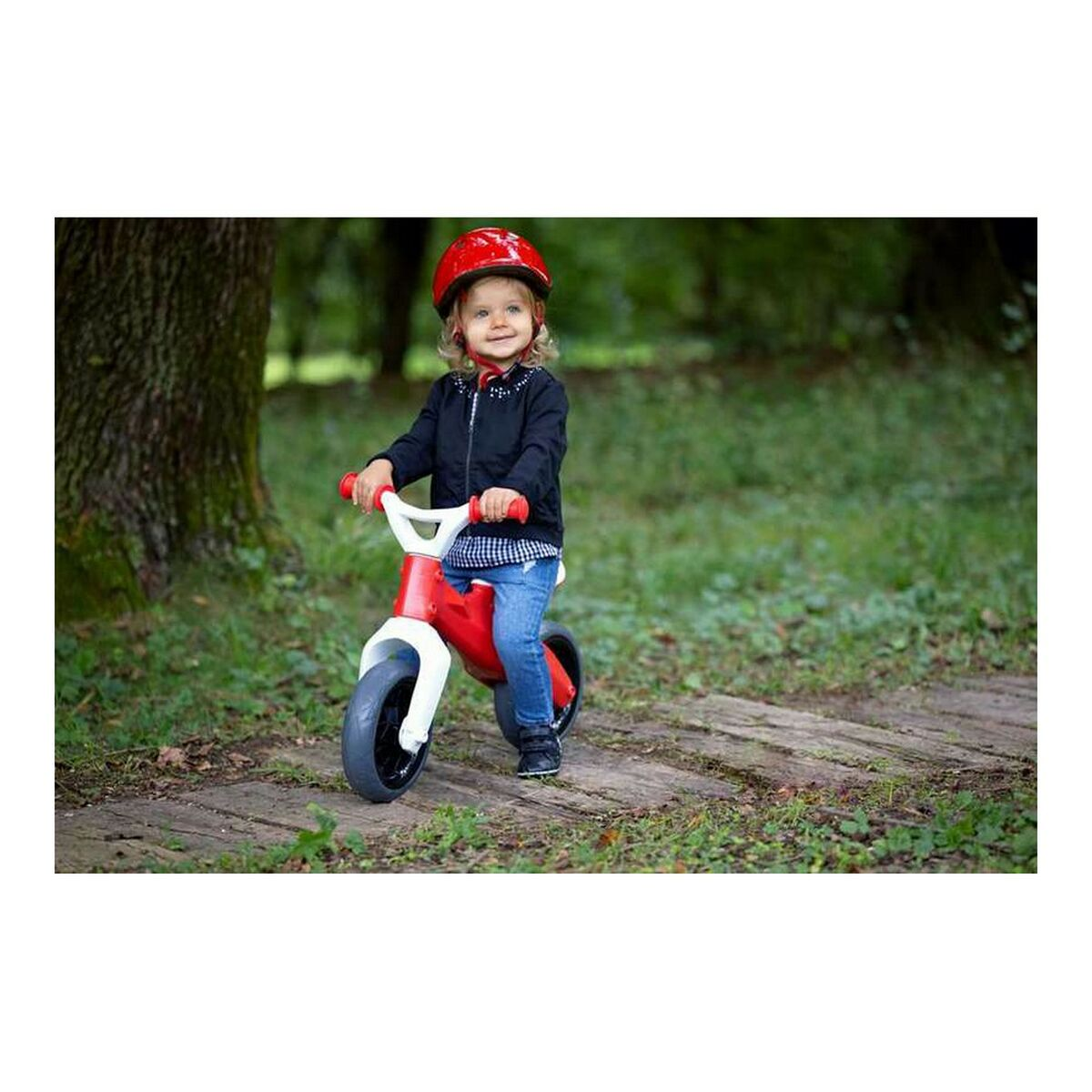 Bambino in bicicletta rossa e bianca su un sentiero erboso. Indossa un casco rosso.