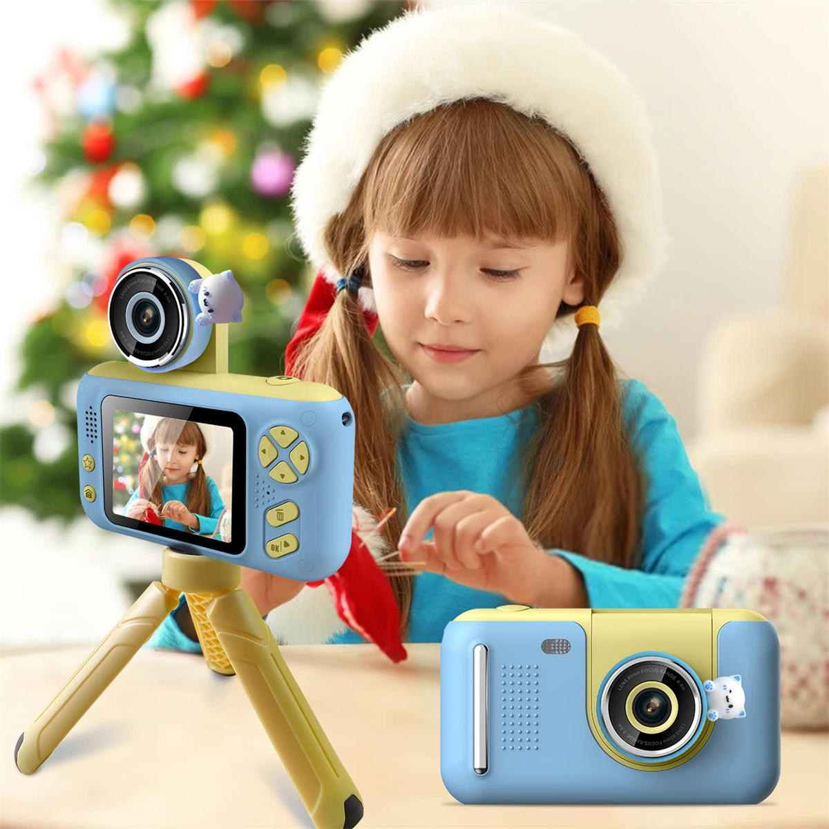 Ein Kind mit Weihnachtsmütze hält eine blau-gelbe Kinderkamera. Weihnachtsbaum im Hintergrund.