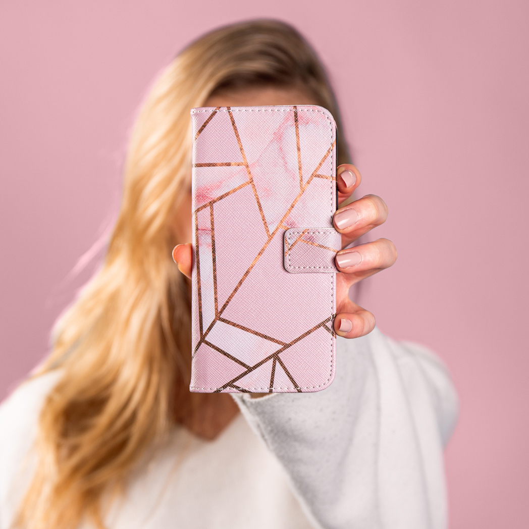 Une femme tient un étui de téléphone rose avec un motif géométrique doré devant son visage.