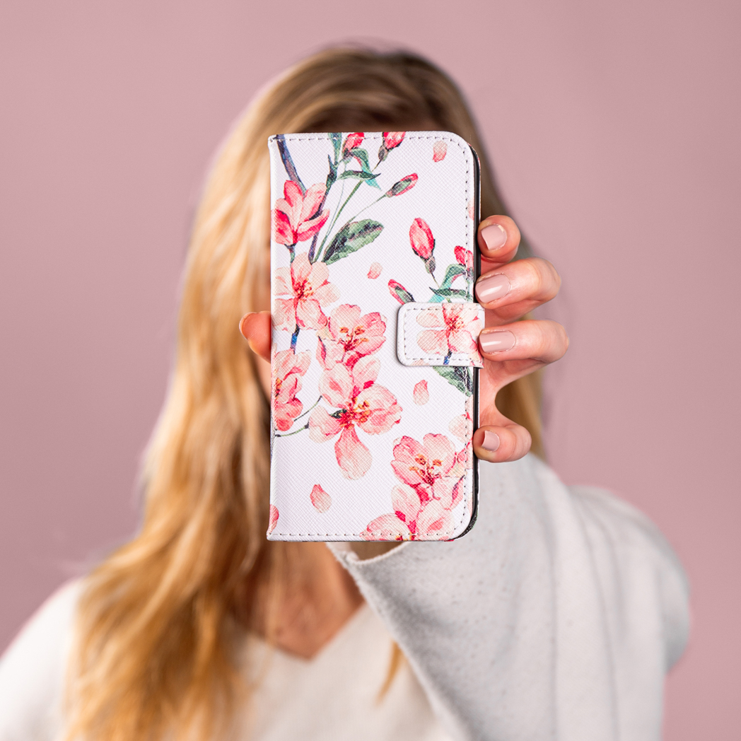 Une personne tenant une coque de téléphone blanche avec un motif floral rose.