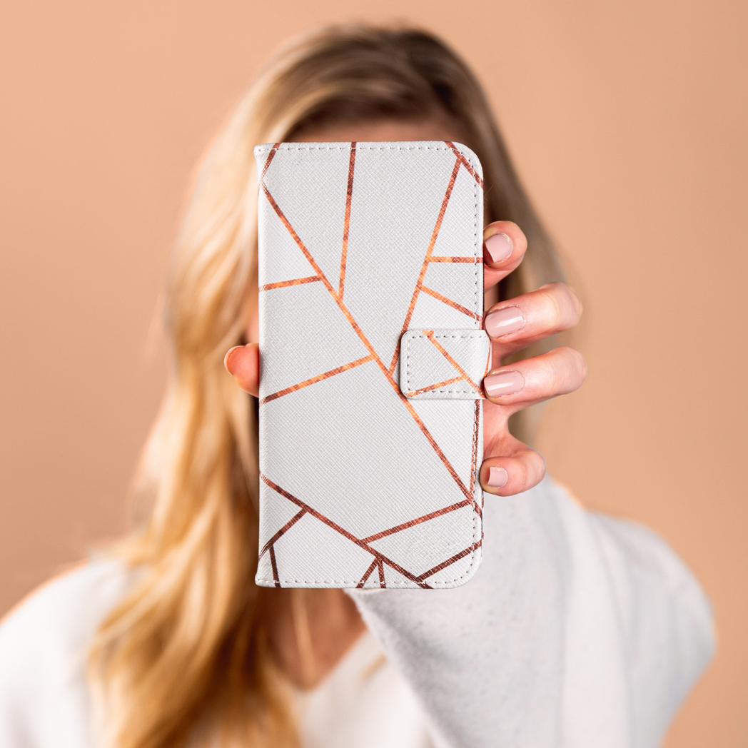 Femme tenant une coque de téléphone avec un motif géométrique blanc et cuivré. Arrière-plan flou.