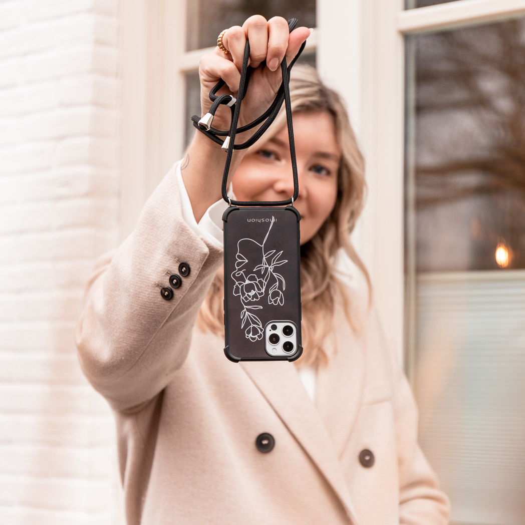 Vrouw die telefoon vasthoudt met hoesje en koord. Bloemen zichtbaar op de hoes.