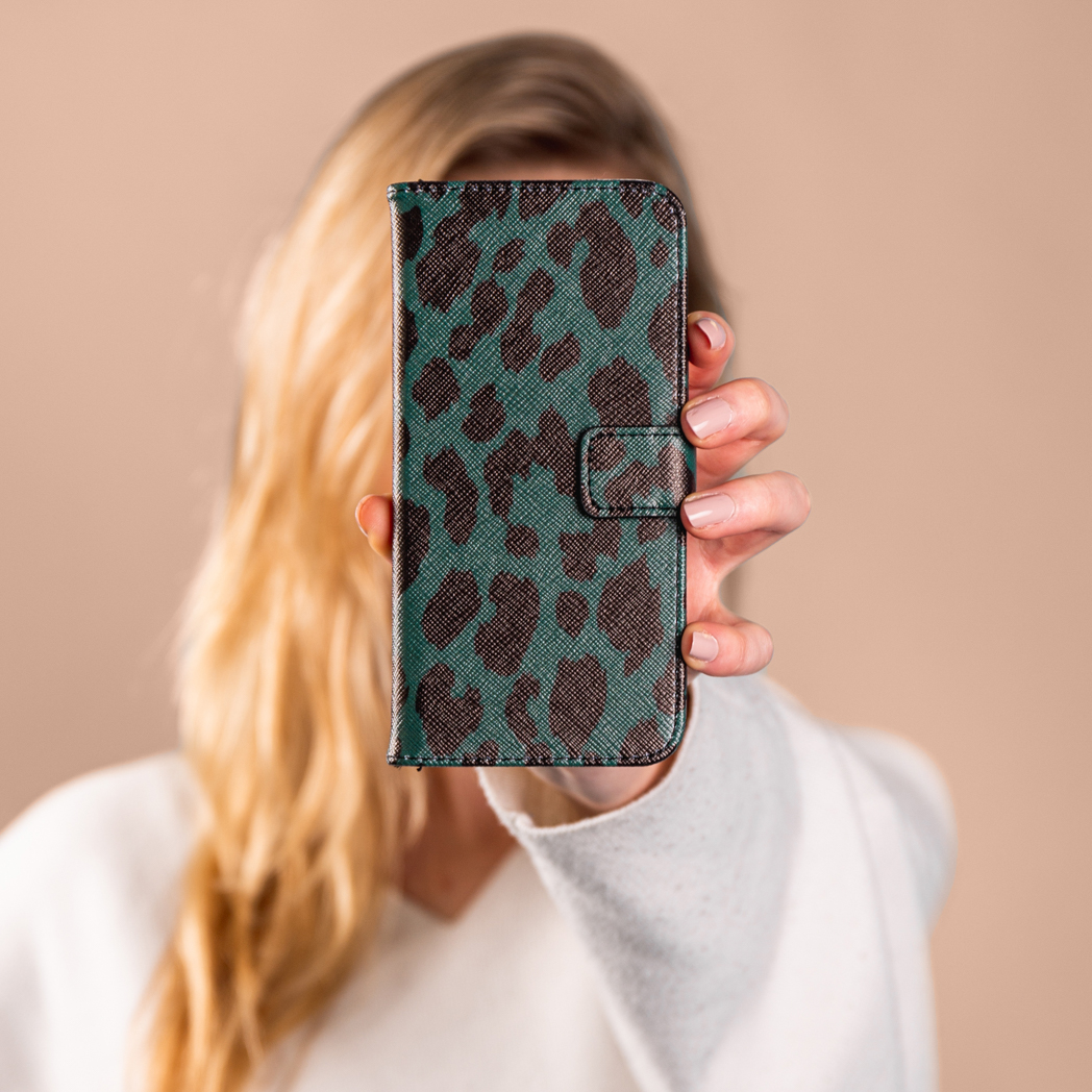 Vrouw houdt een telefoonhoesje vast met een blauwgroen en bruin patroon. Achtergrond: beige.
