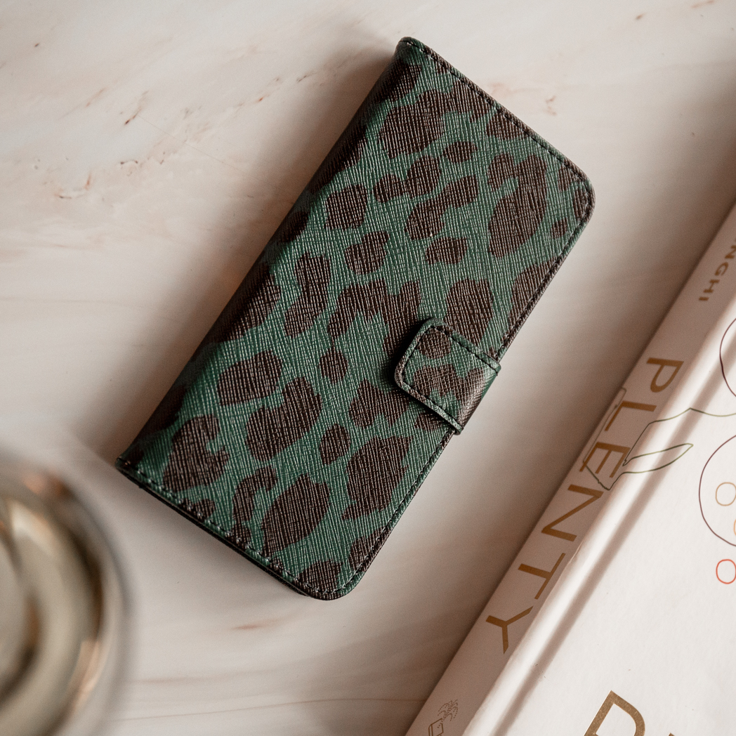Telefoonhoesje met blauwgroen en bruin patroon op een marmeren oppervlak, met een tijdschrift.