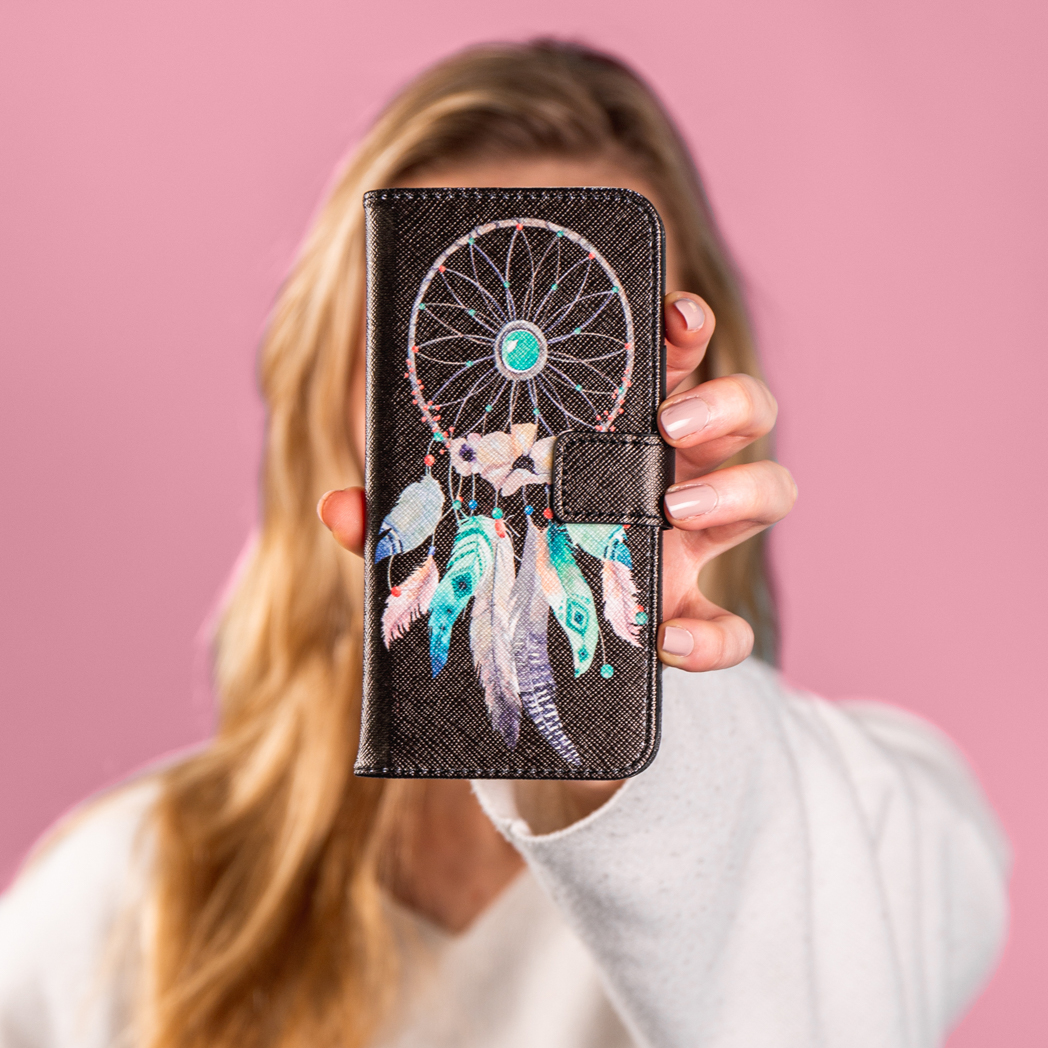 Femme tenant un étui de téléphone avec un motif attrape-rêves. Fond : rose.