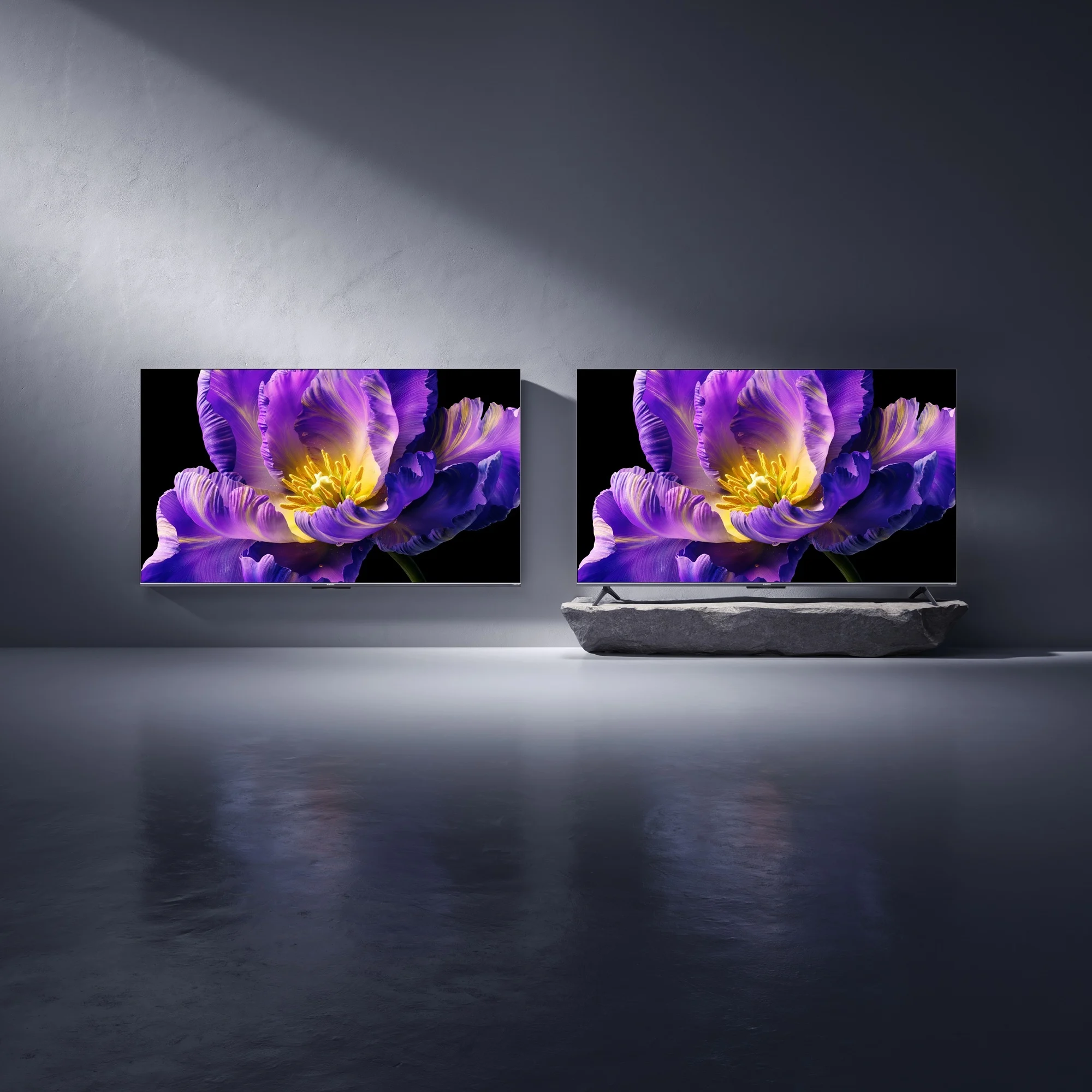 Dwa telewizory wyświetlają fioletowy kwiat na szarym tle ściany i podłogi w ciemnym, nowoczesnym otoczeniu.
