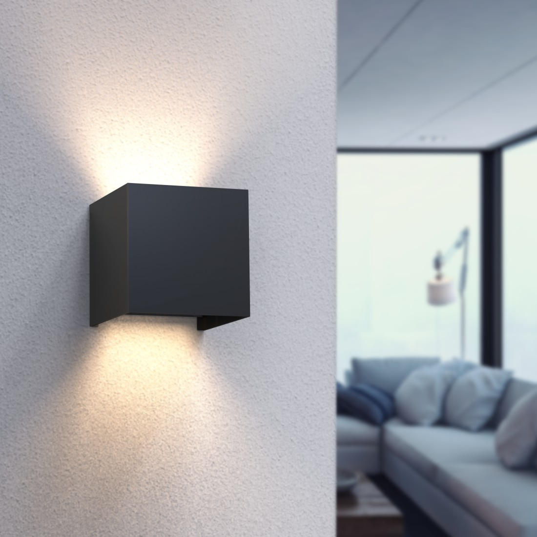 Schwarze quadratische Wandleuchte, die Licht nach unten projiziert. Die Wand ist weiß, der Hintergrund unscharf.