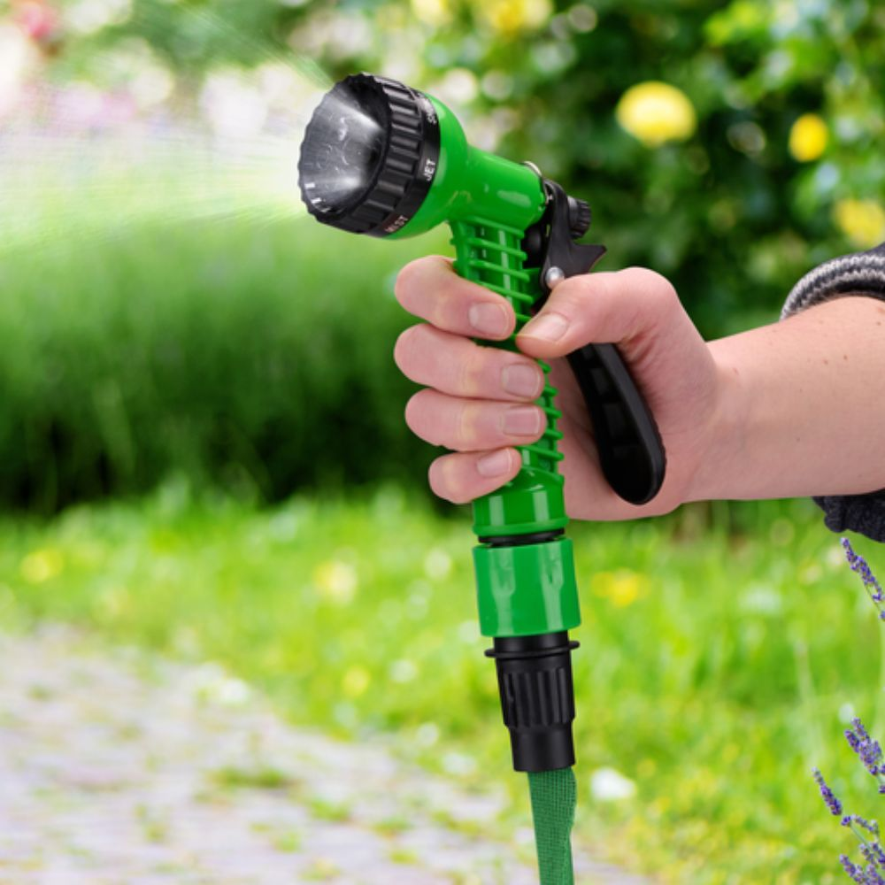 Hand die een groene en zwarte tuinslangmond vasthoudt. Water sproeit. Groene gras achtergrond.