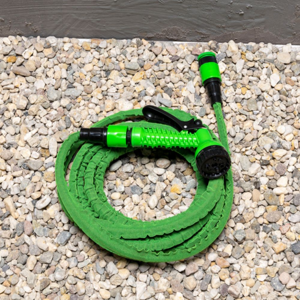 Een groene tuinslang opgerold op een bed van kleine kiezels. De slang heeft een groen en zwart mondstuk.