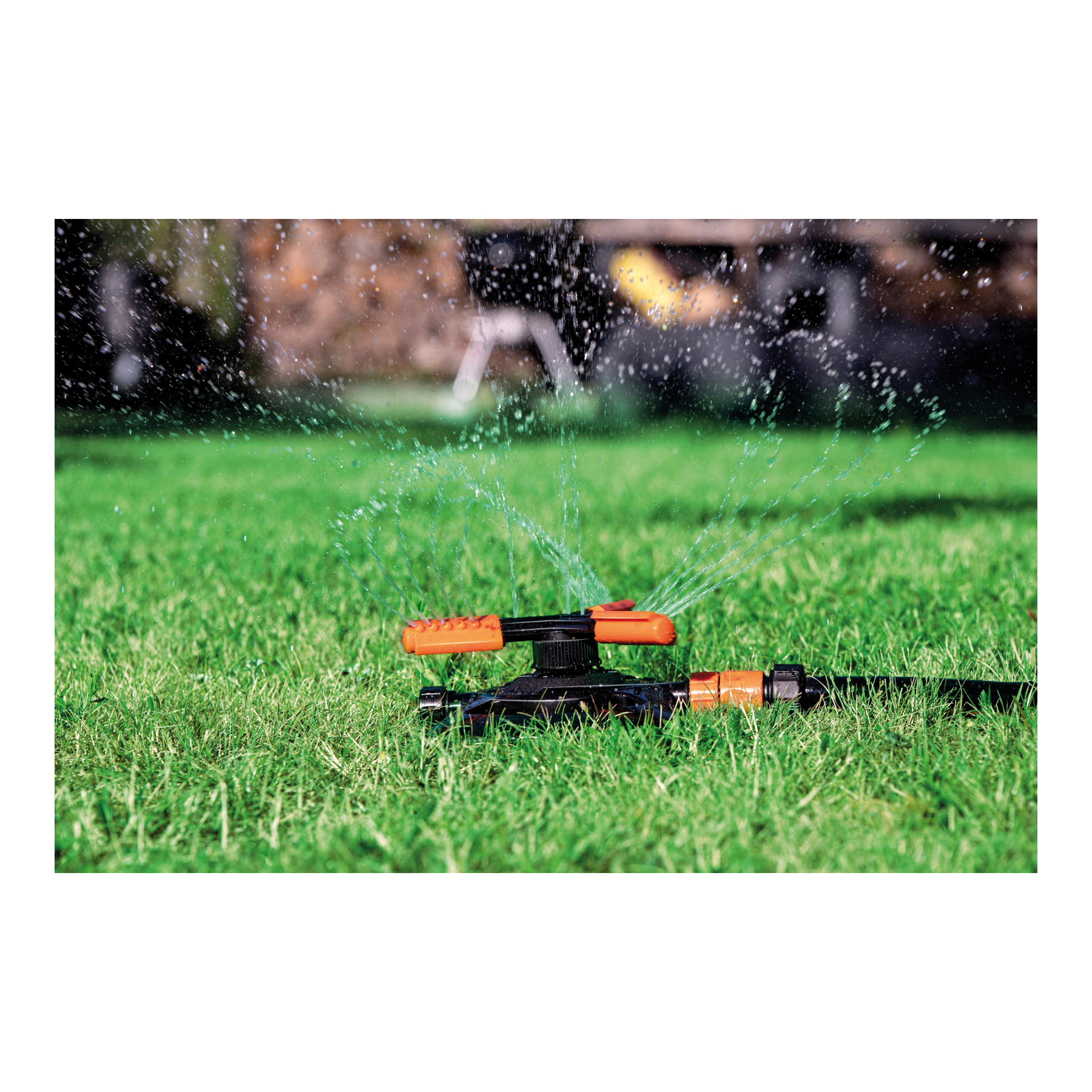 Een sproeier die water sproeit op groen gras. De sproeier is zwart en oranje.