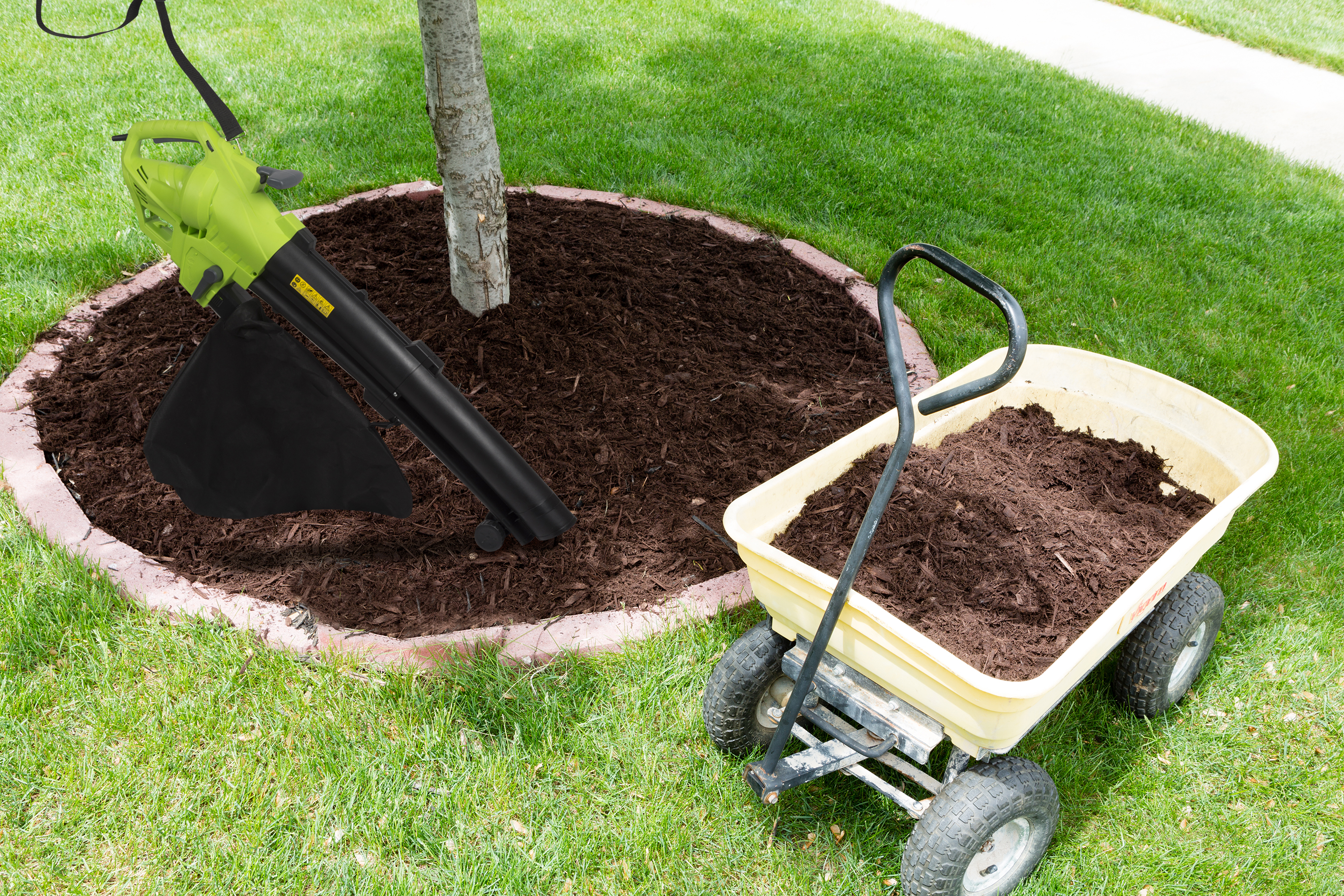 Een bladblazer en een tuinkar met mulch op groen gras.