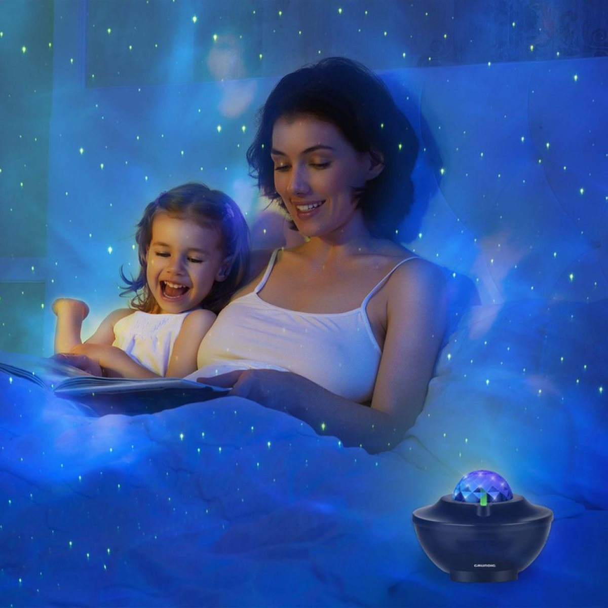 A mother and child in bed, looking at a book. A galaxy projector shines stars onto them.