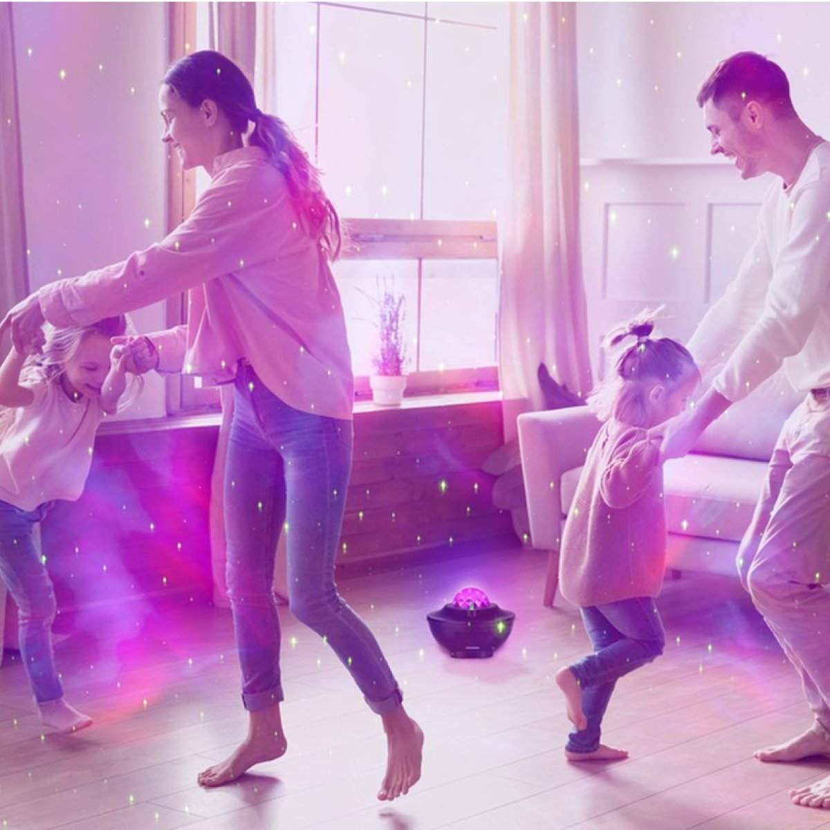 Family dancing in a room with a galaxy light. Two adults and two children are dancing.