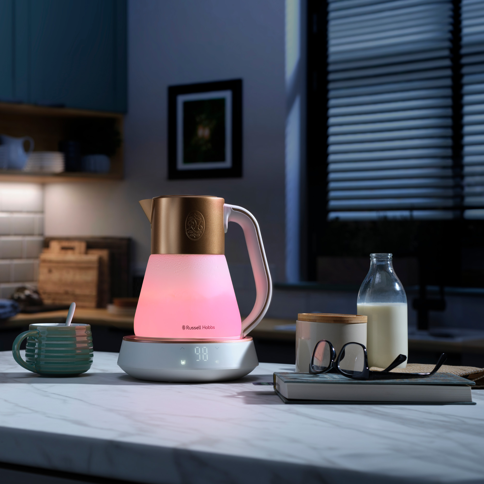 Un bollitore elettrico illuminato su un piano di lavoro, con una tazza, occhiali, un libro e una bottiglia di latte. Cucina sullo sfondo.