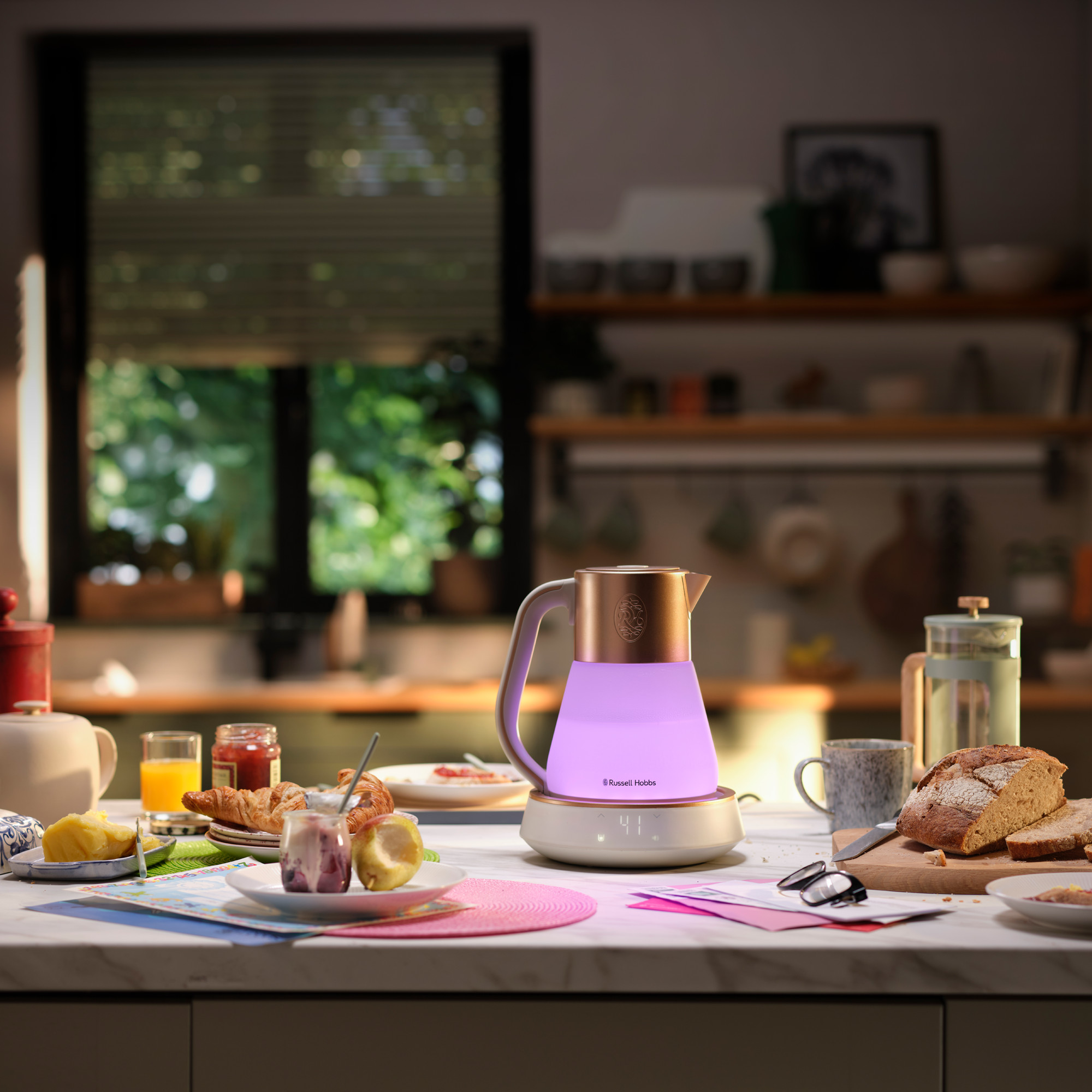 Scena di cucina con un bollitore e cibo sul tavolo. Una finestra sullo sfondo, con la luce del giorno.