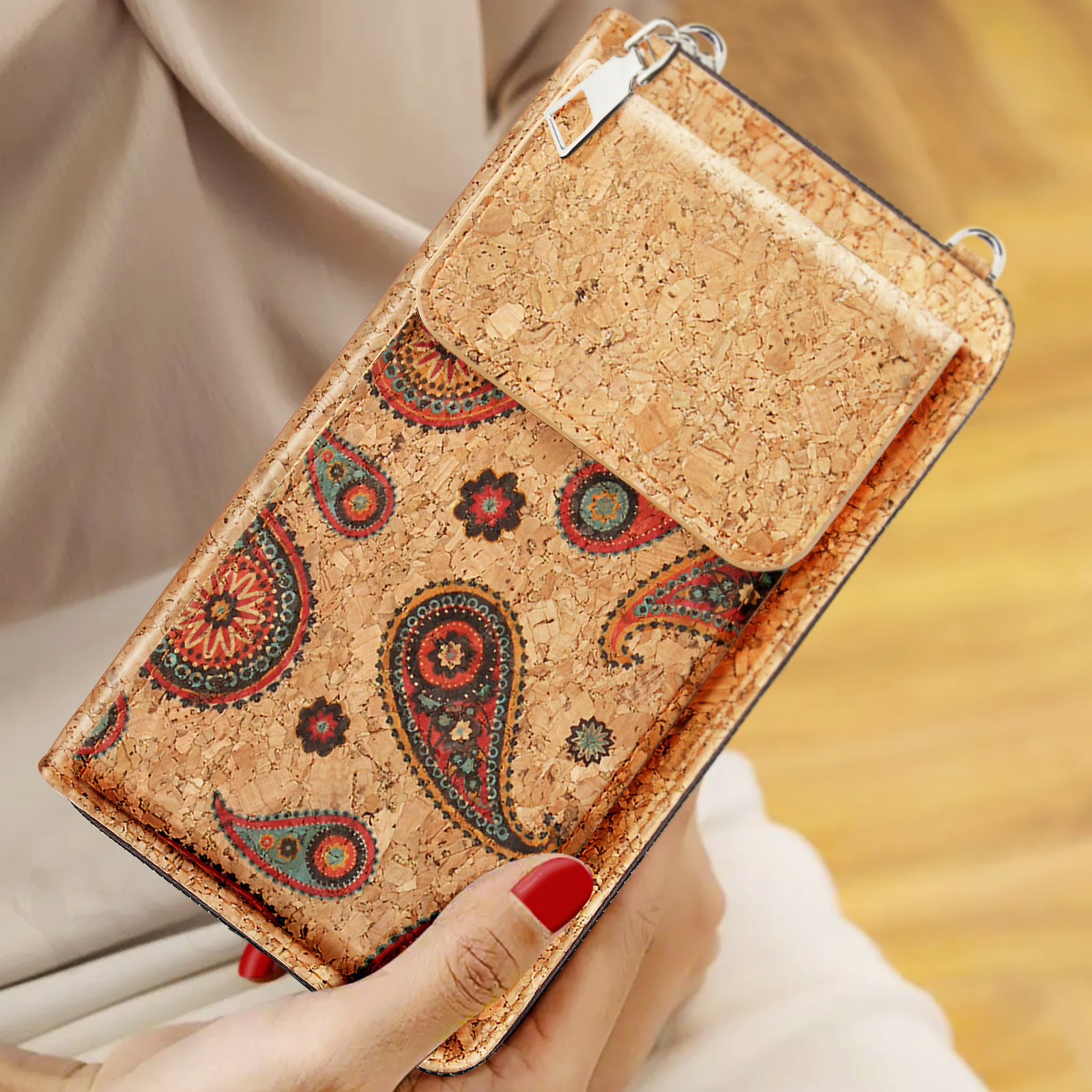 Eine Handy-Geldbörse mit Korkmuster und Paisley-Design wird von einer Person gehalten. Ein roter Nagel wird gezeigt.