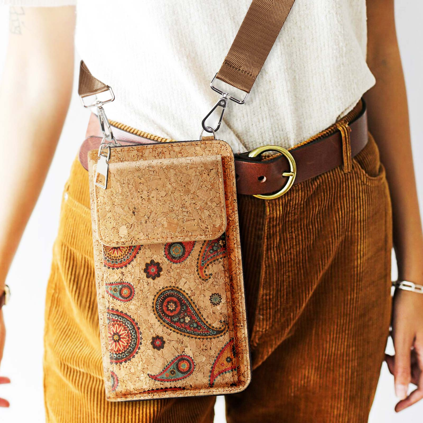 Person trägt eine Kork-Handyhülle-Umhängetasche mit Paisley-Design. Braune Cordhose und ein Gürtel.