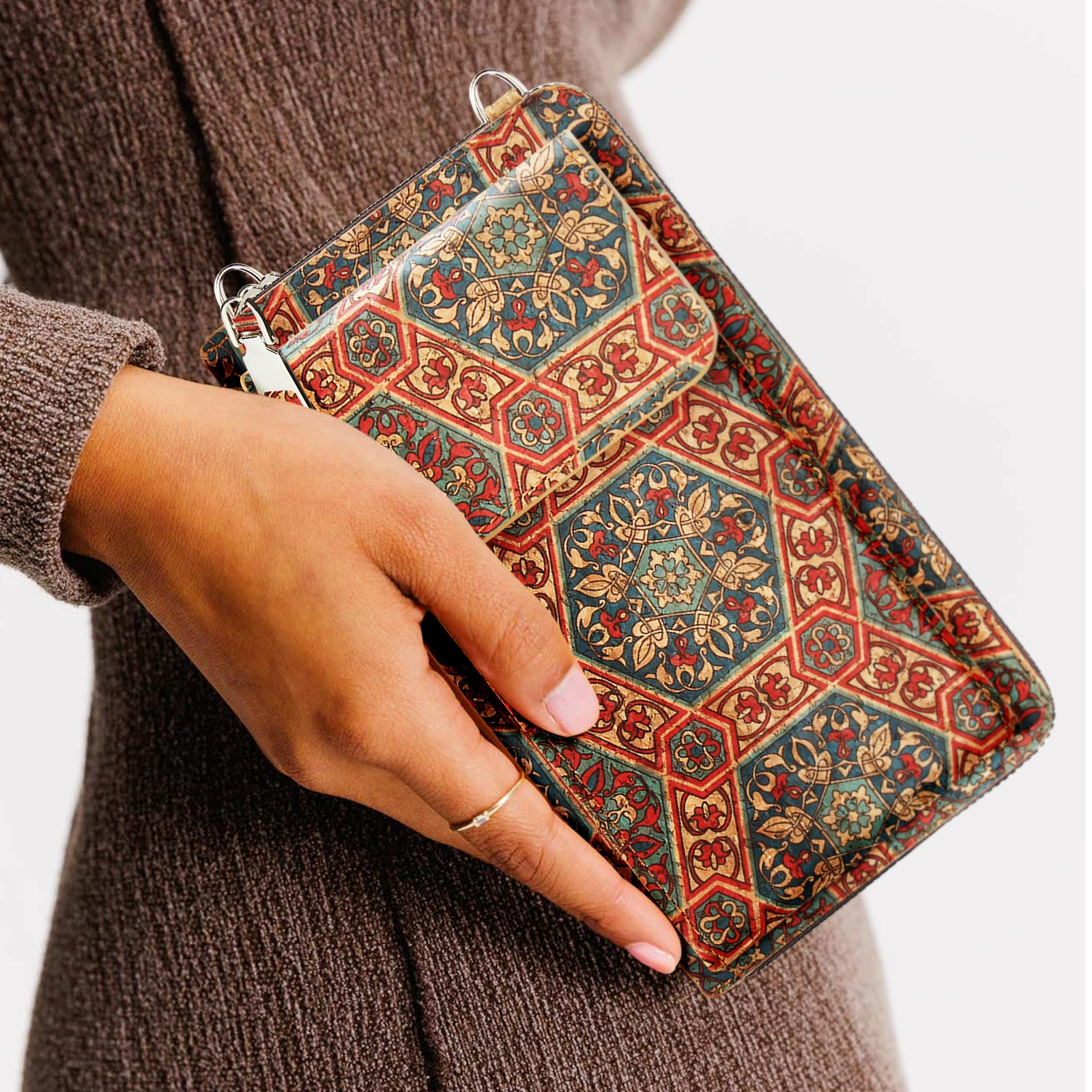Eine Person hält eine gemusterte Tasche mit einem kleinen Beutel. Die Tasche hat rote, blaue und goldene Muster.