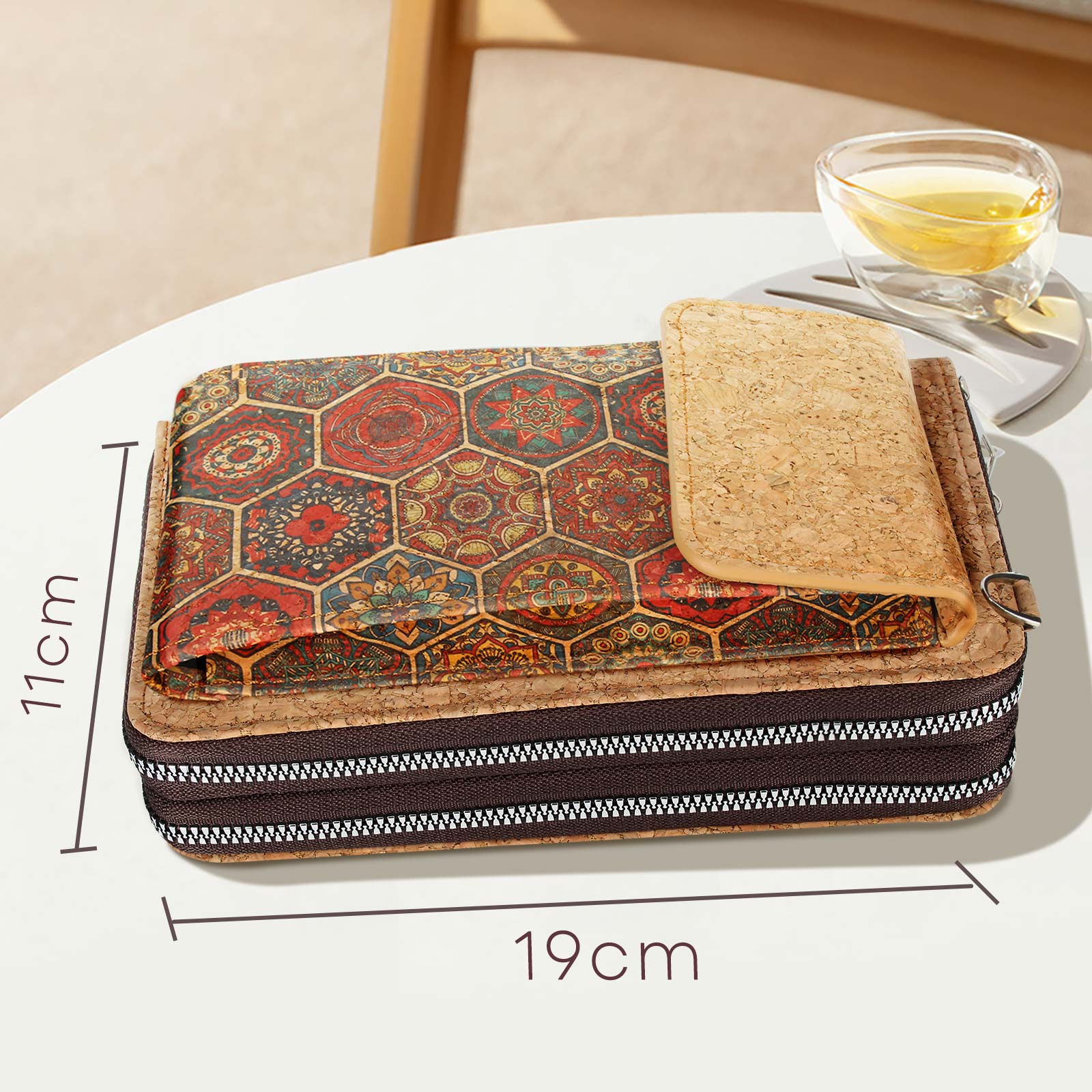 Eine Korkbrieftasche mit gemusterter Oberseite und Reißverschluss. Teetasse ist an der Seite. Text: 11cm x 19cm.