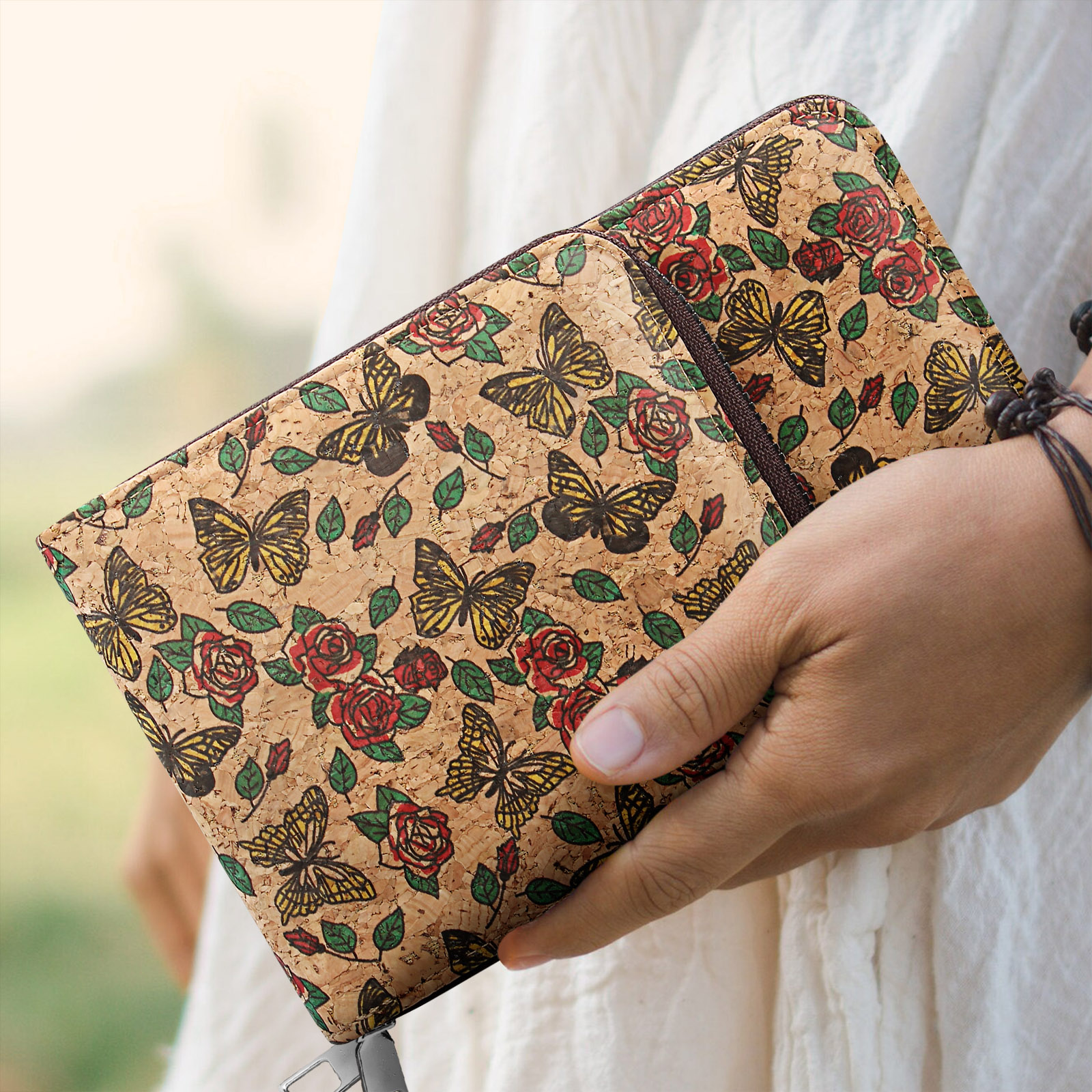 Kork-Notizbuch mit Schmetterlingen und Rosen. Hand hält es. Braunes, rotes Blumendesign.