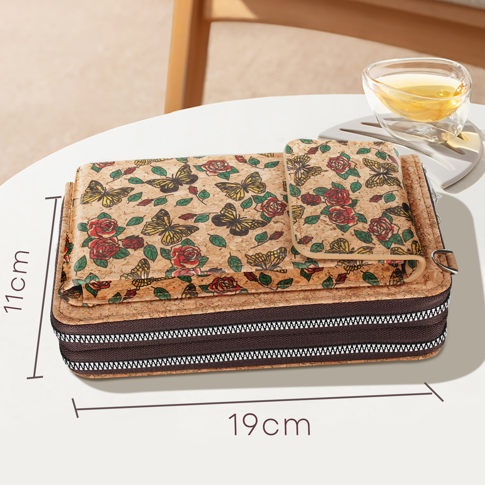 Ein Korketui mit floralem Design liegt auf einer weißen Oberfläche. Eine Tasse Tee ist in der Nähe. Maße sind 11x19cm.