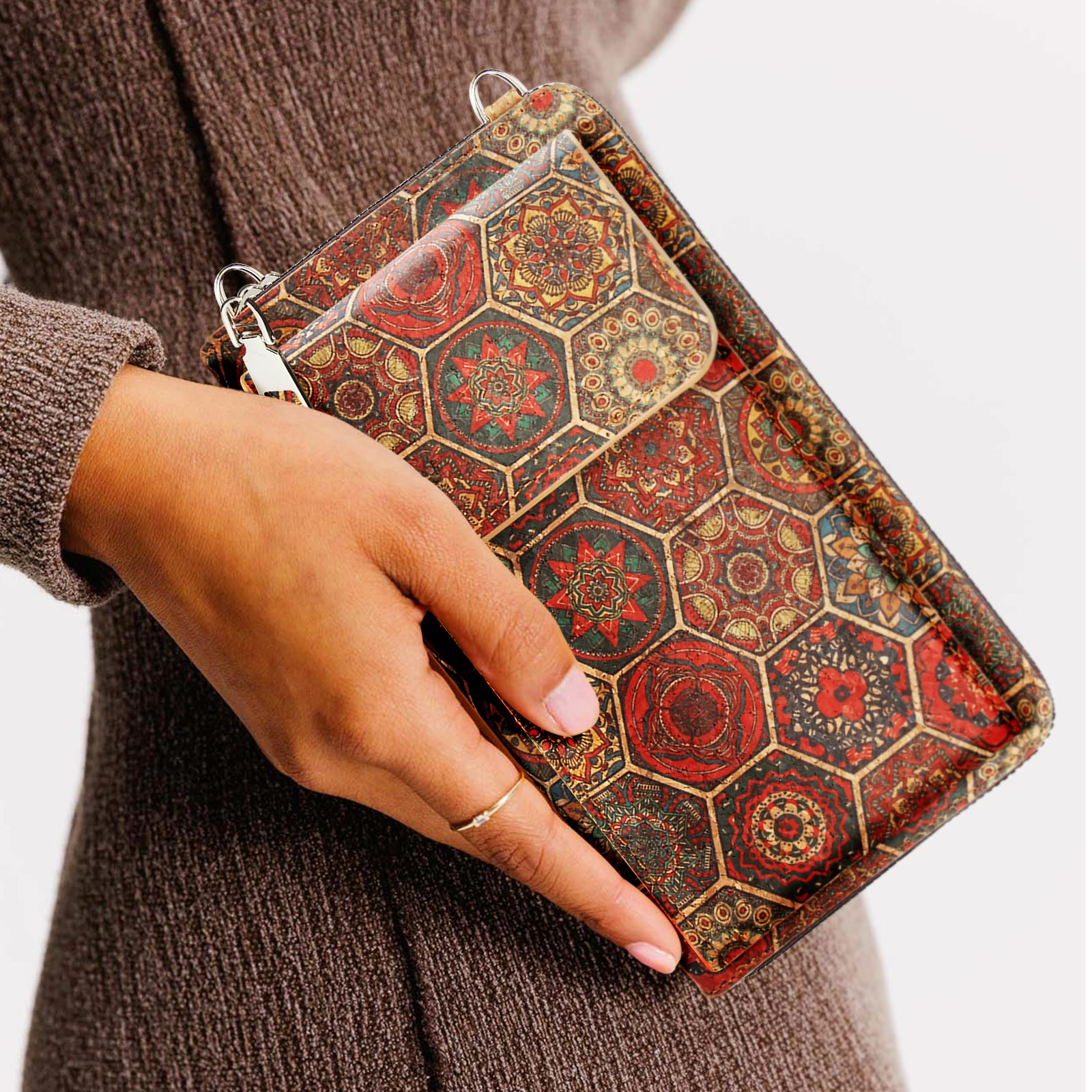 Eine Frau hält eine gemusterte Geldbörse mit einem kleineren Beutel. Die Geldbörse hat ein Mosaikdesign in Rot, Braun und Grün.