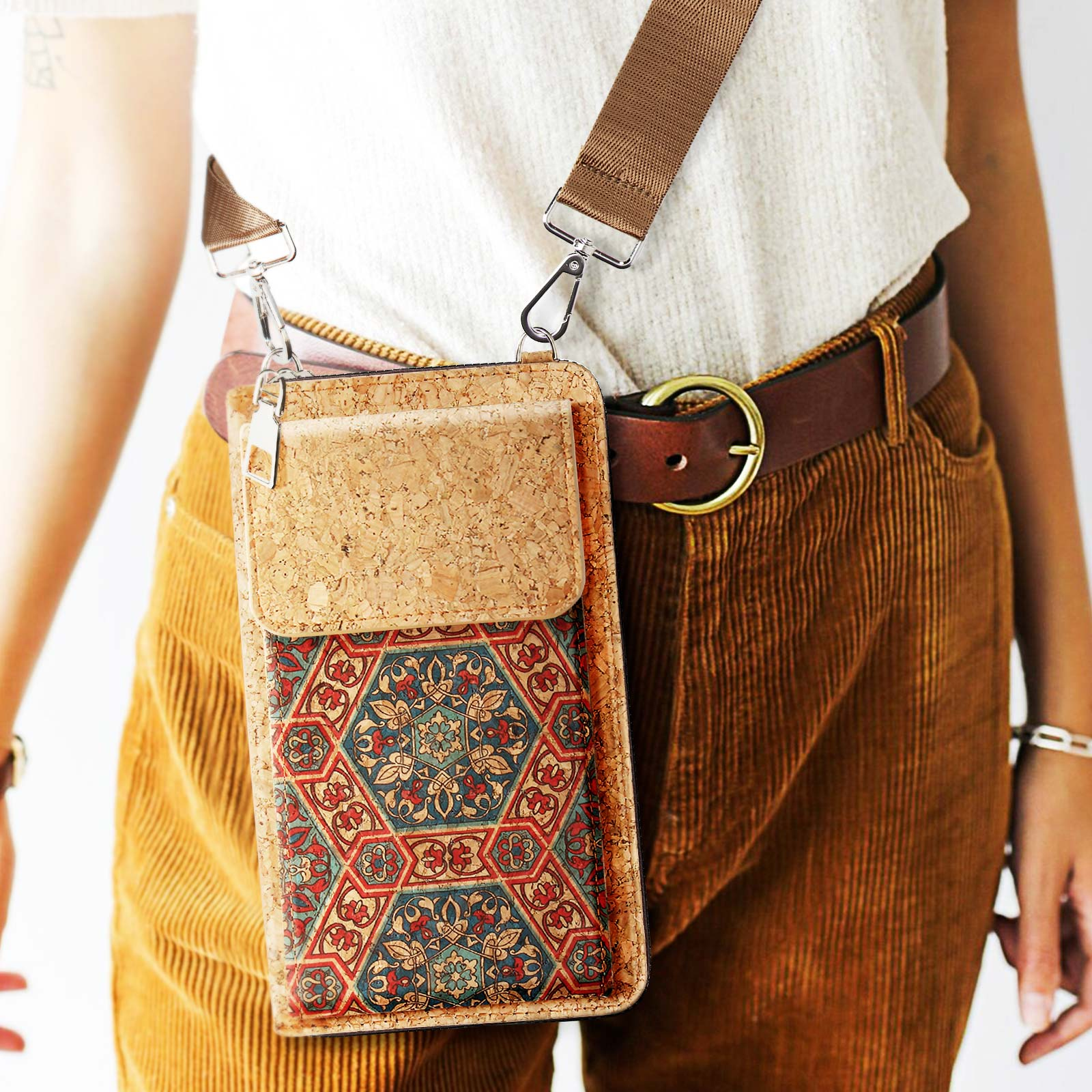 Person trägt eine Crossbody-Telefontasche mit floralem Muster und Cordhose. Brauner Gürtel.