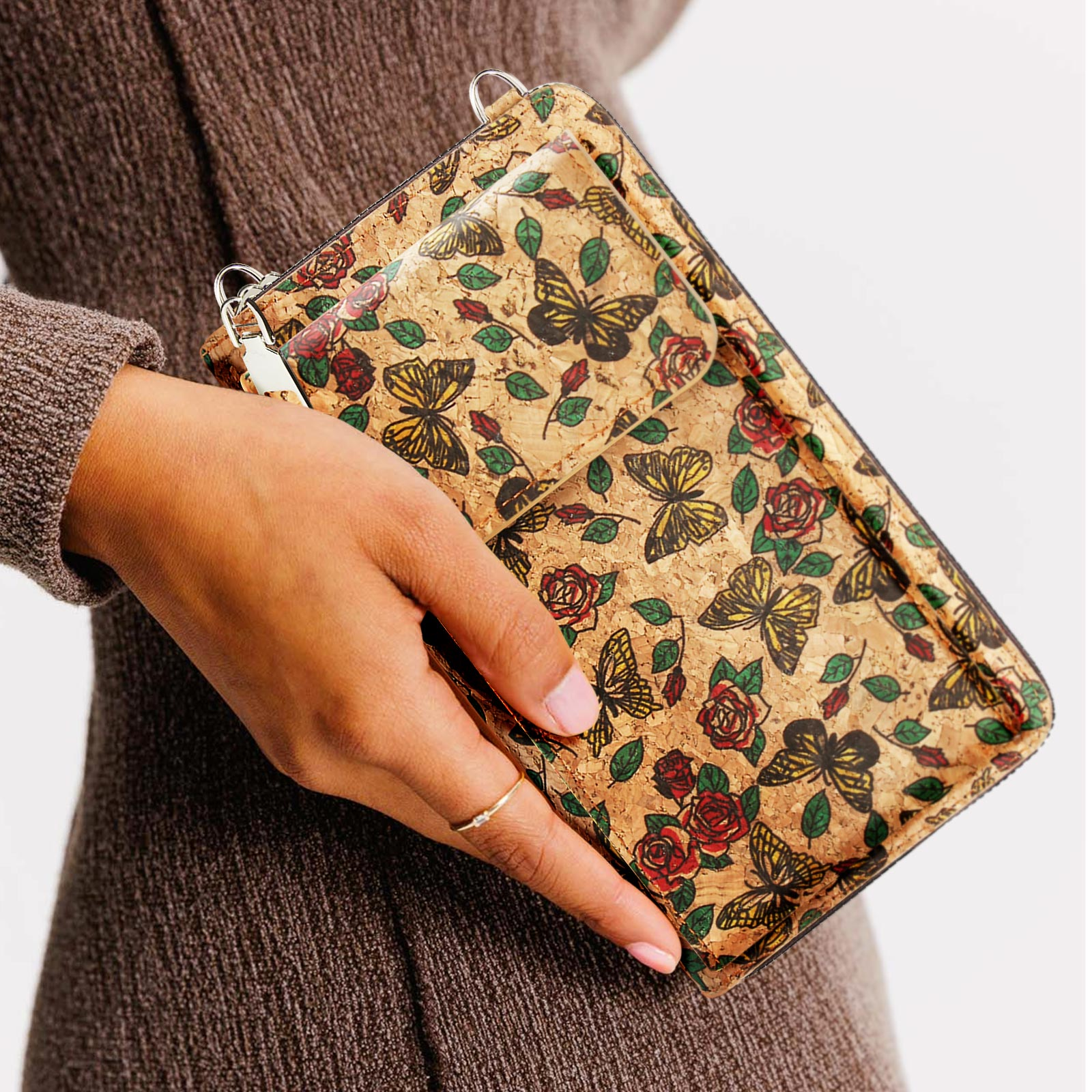 Frau hält eine Korkbrieftasche mit Schmetterlingen und Rosen vor weißem Hintergrund.