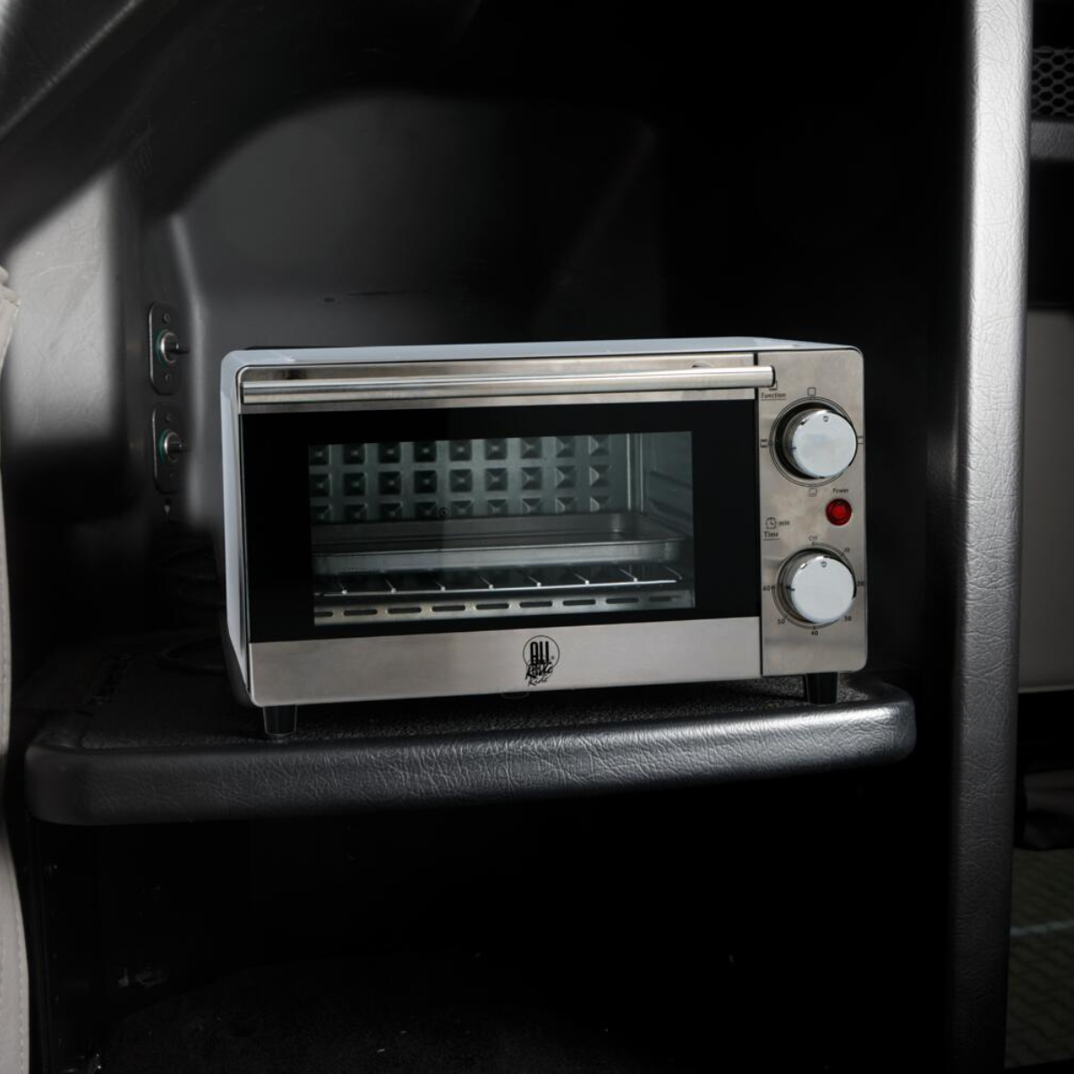 Un forno tostapane argento e nero è appoggiato su una mensola in uno spazio buio, con una porta in vetro e manopole di controllo.