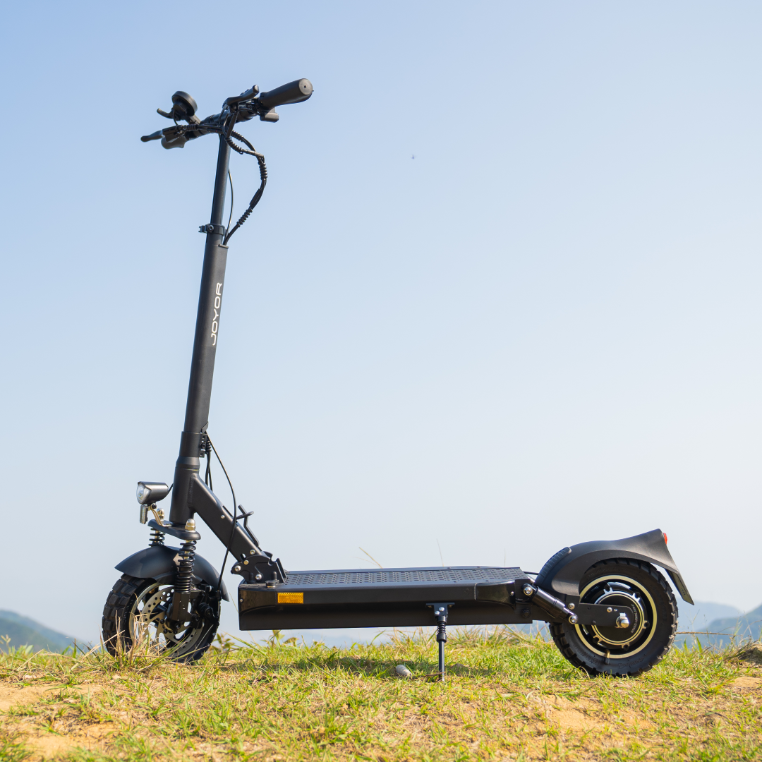 Schwarzer Elektroroller auf Gras, mit blauem Himmel im Hintergrund. Ein entfernter Berg ist sichtbar.