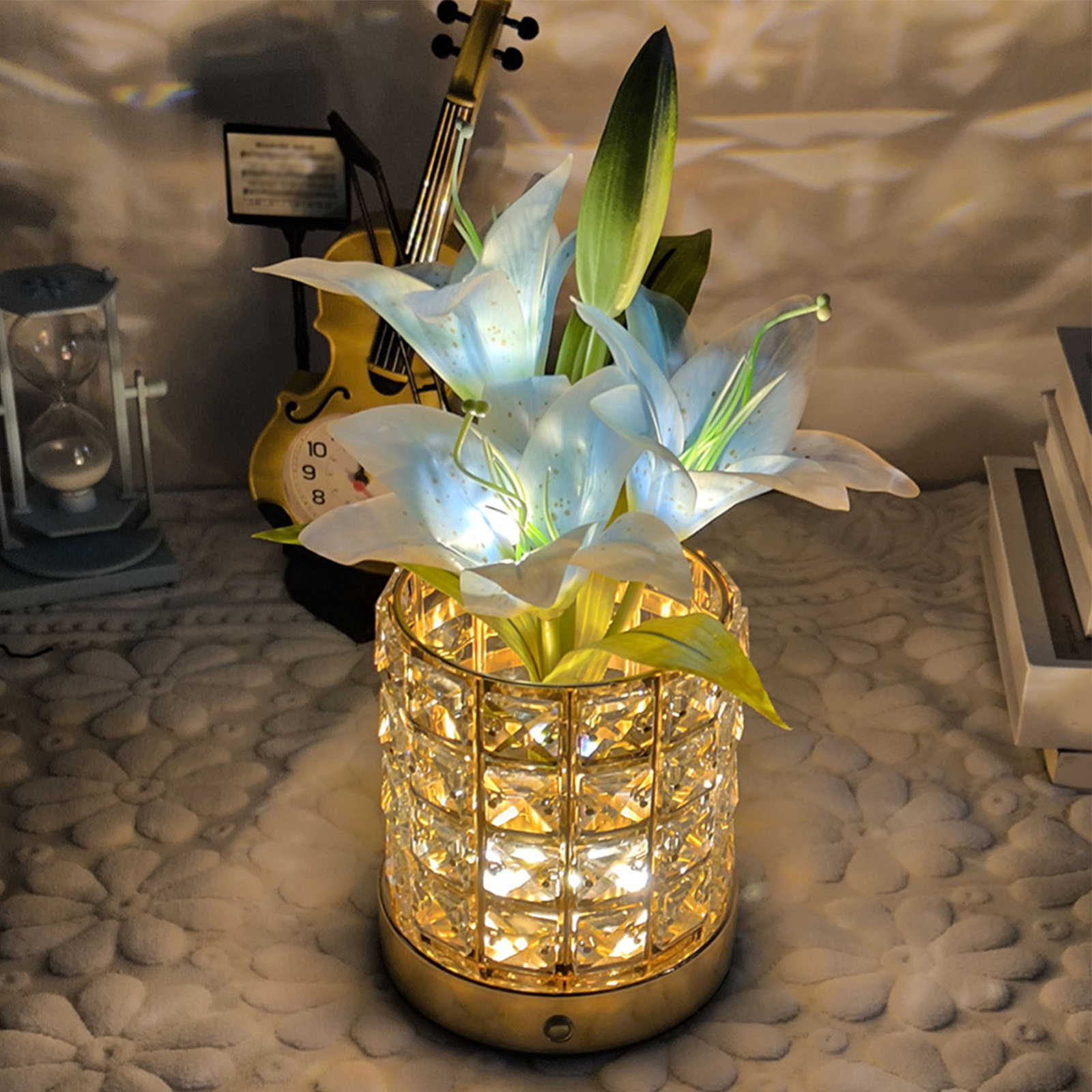 Eine beleuchtete Kristallvase mit blauen Blumen und einer Geige im Hintergrund auf einem weißen Tisch.