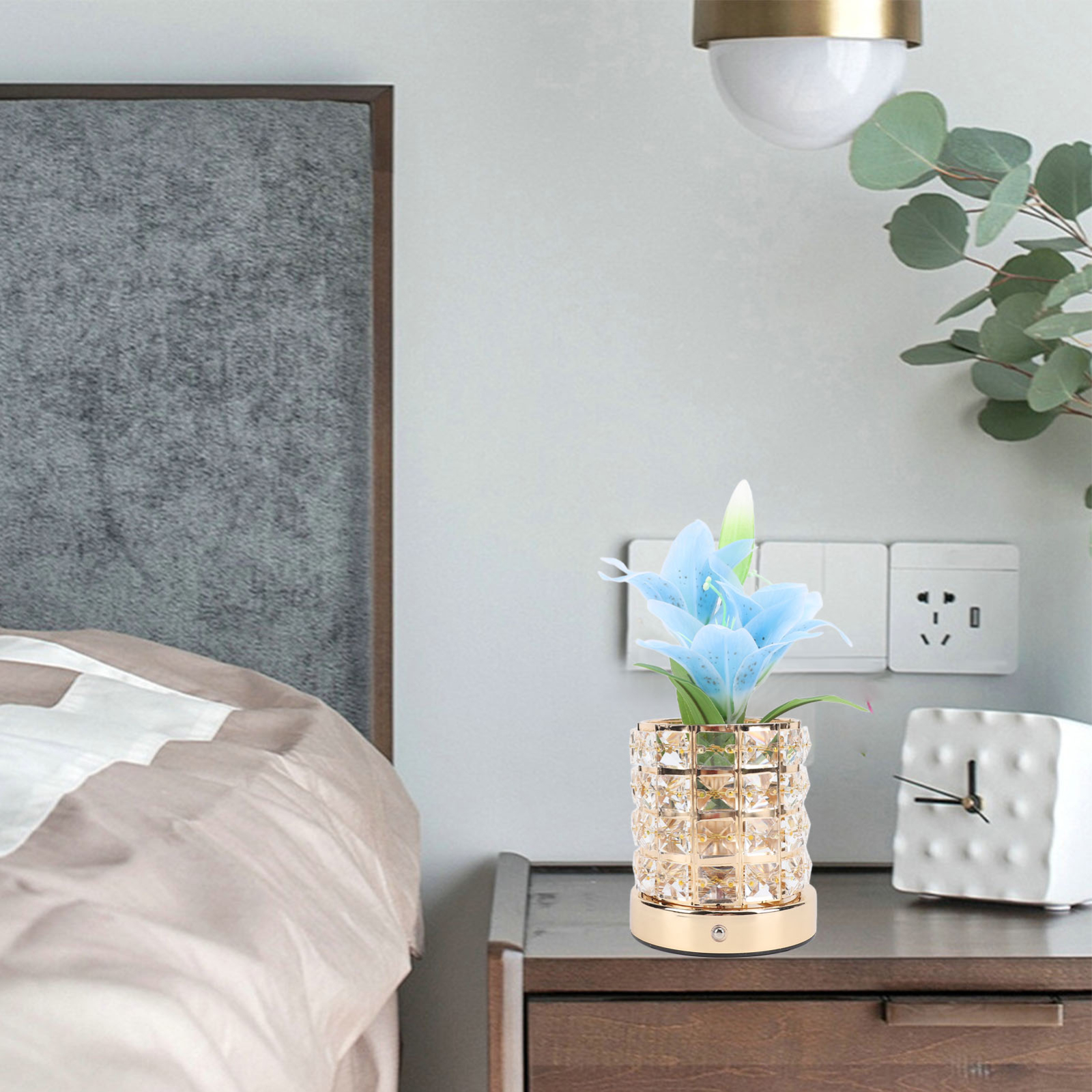 Eine dekorative Blumenvase mit blauen Blumen auf einem Nachttisch, neben einem Bett und einer Uhr.