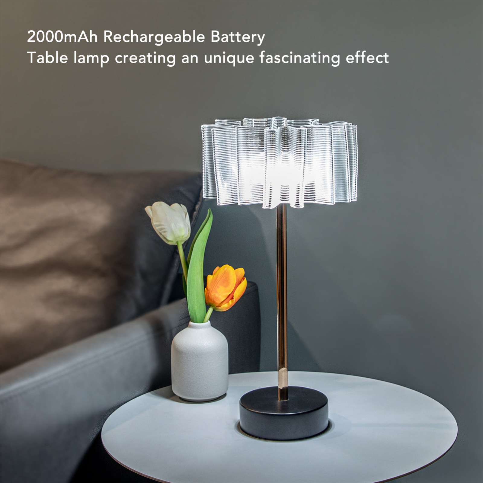 Eine Lampe mit weißem Schirm und schwarzem Sockel, neben einer Vase mit Blumen auf einem Tisch.