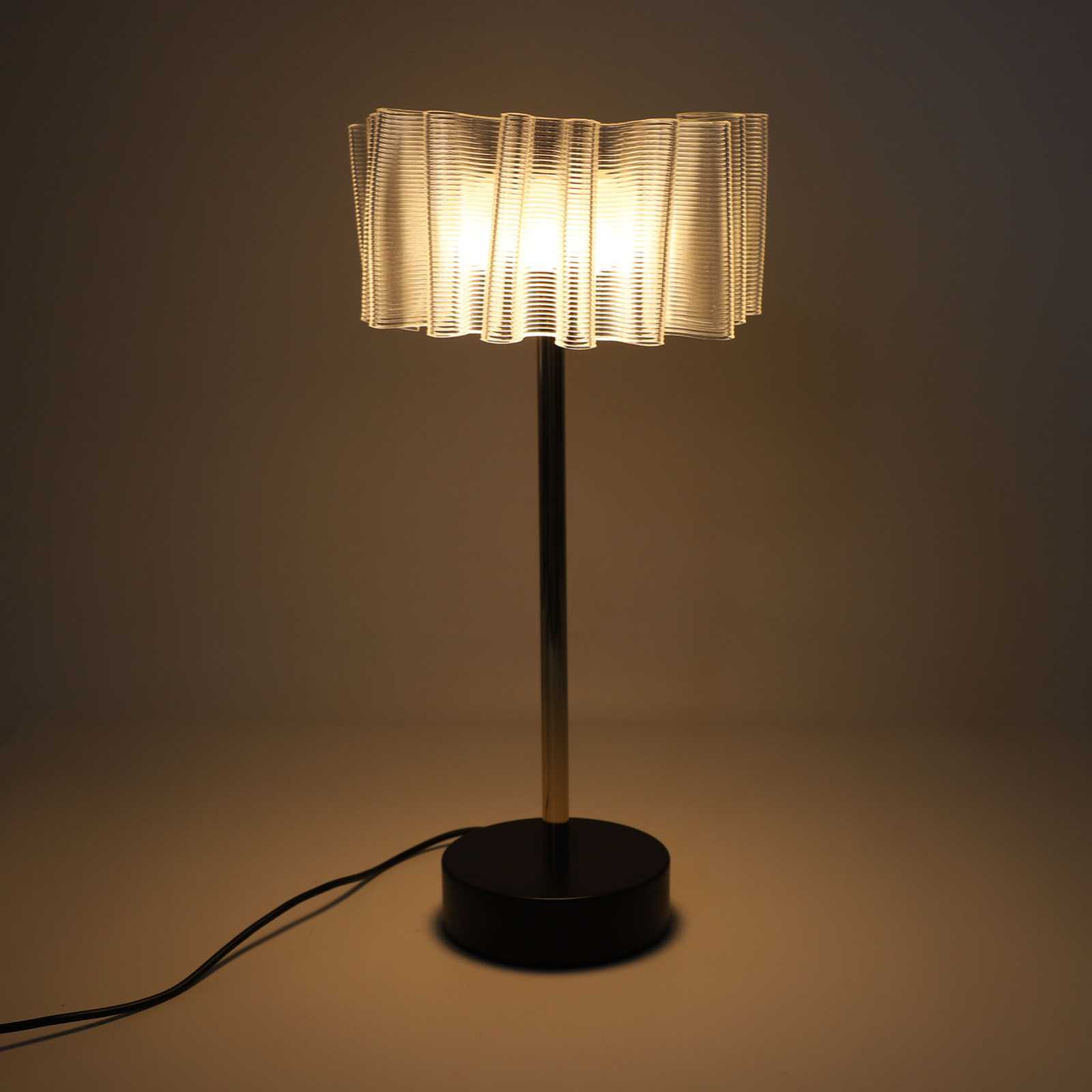 Moderne Lampe mit dekorativem Schirm und schwarzem Fuß. Das Licht ist an.