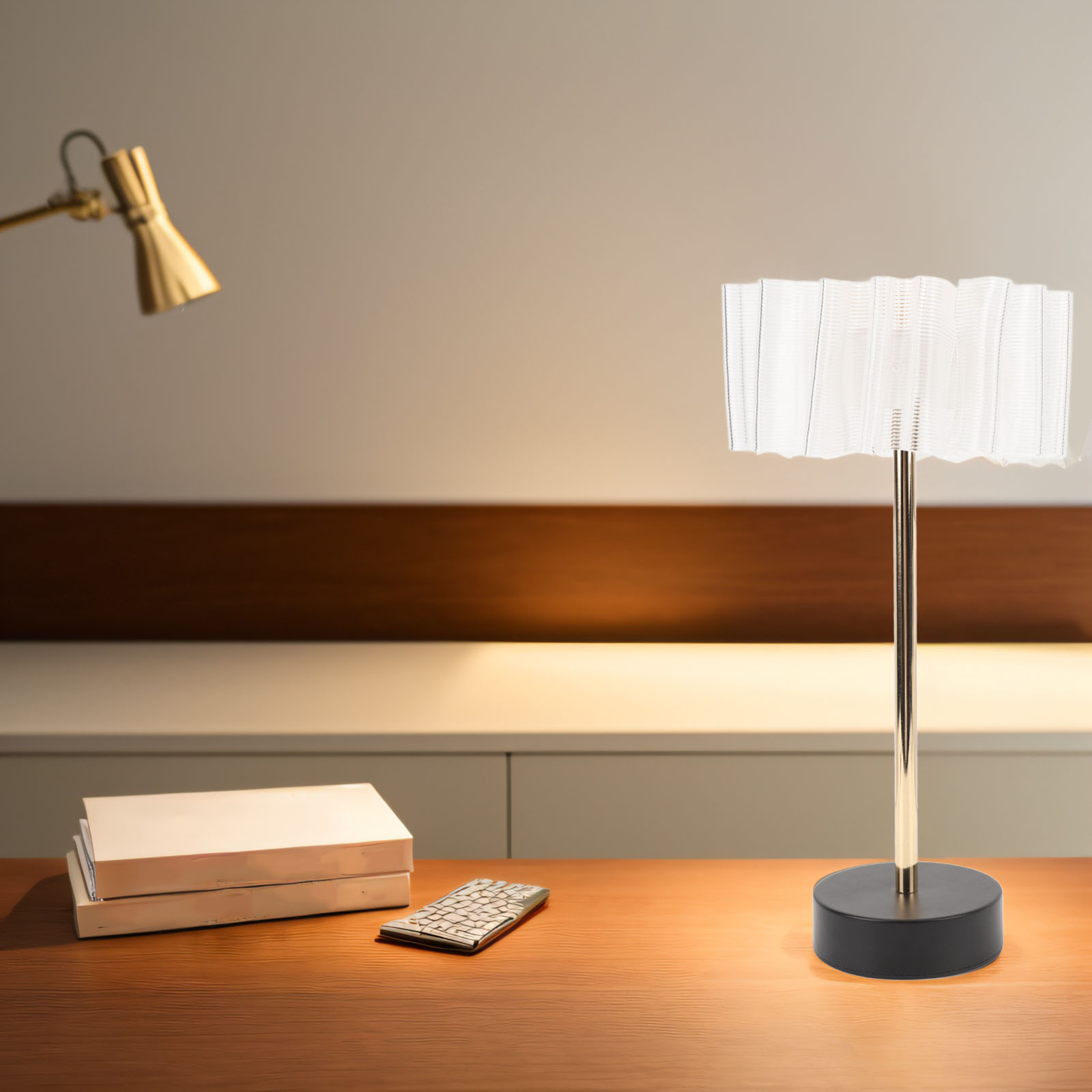 Eine Tischlampe mit weißem Schirm und goldenem Schaft auf einem Holztisch, Bücher und eine Fernbedienung.