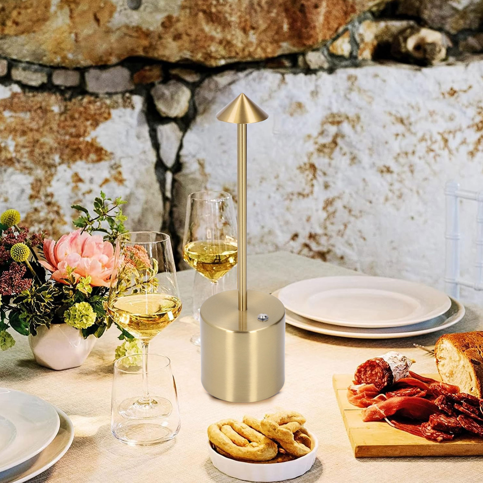 Ein Tisch mit Lampe, Blumen, Weingläsern und Essen. Die Szene ist im Freien.